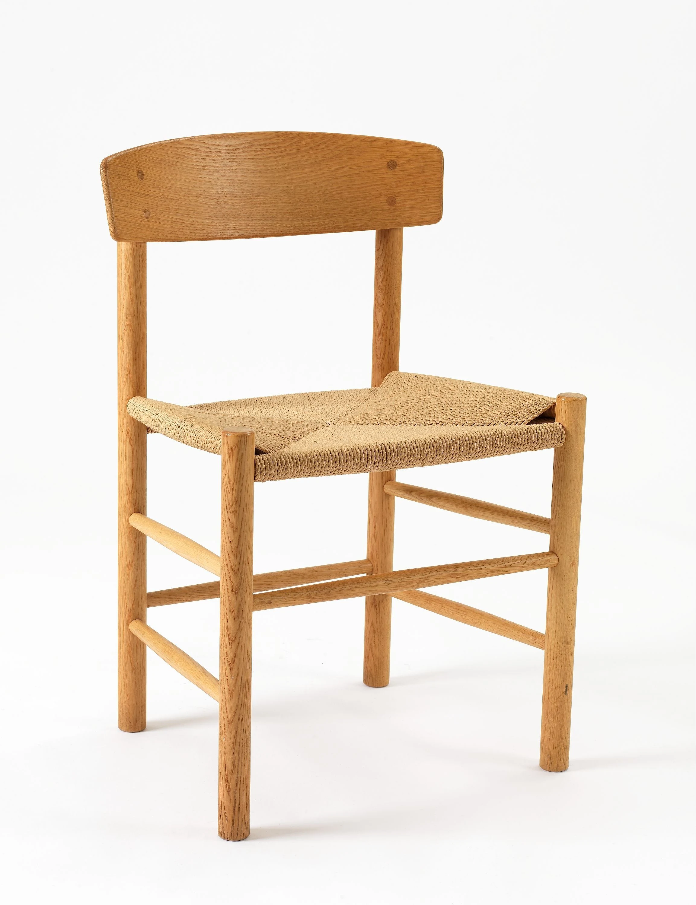 Three-quarter view of a J39 chair with round timber legs and stretchers, a broad curved wooden back and a natural paper-cord seat.
