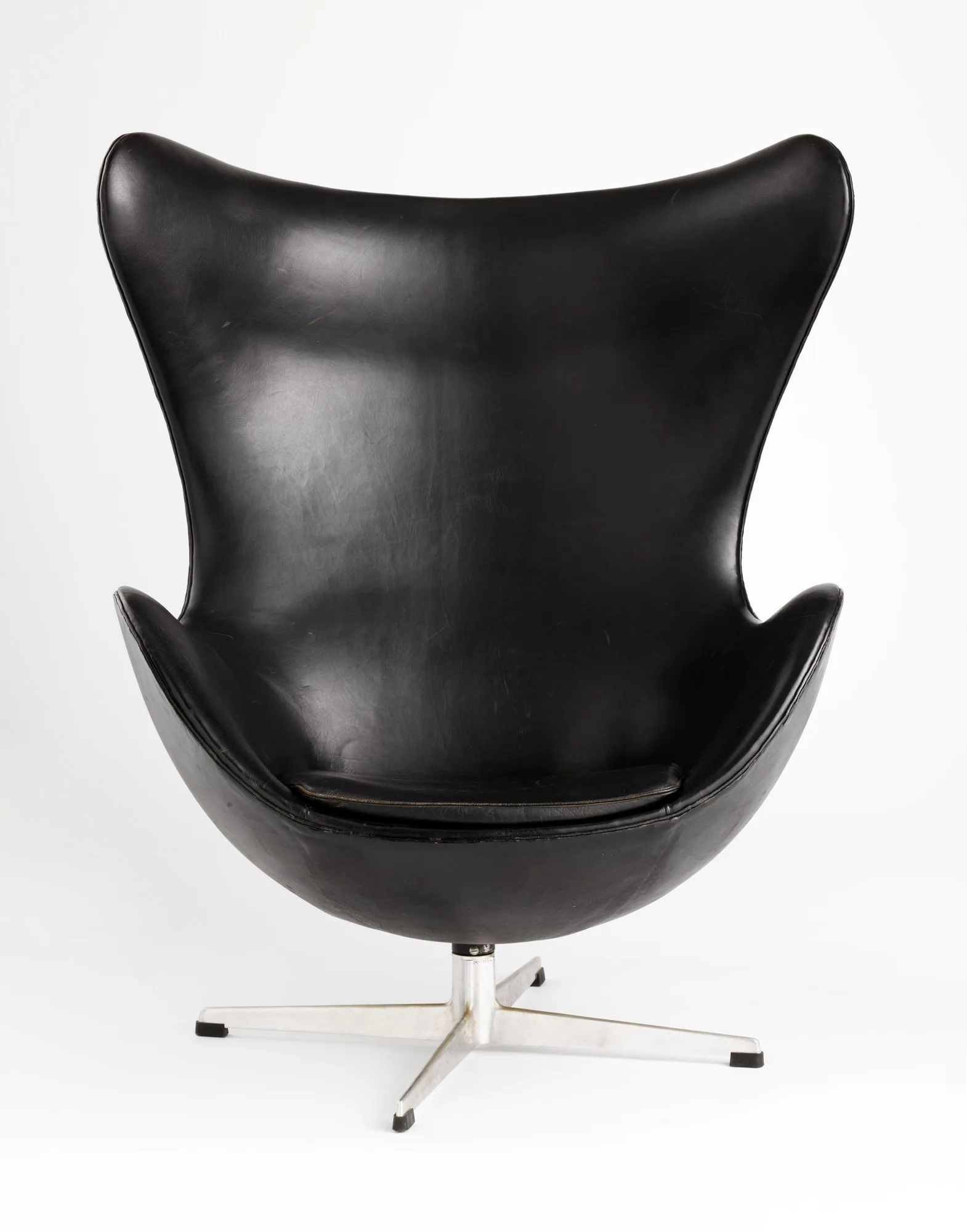A frontal view of a black leather Egg Chair whose high curving wings narrow to a central stem and aluminium star base.