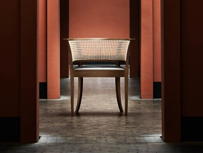 A Faaborg Chair centred in a red museum passage, with a dark timber frame, open cane back and slender tapering legs.