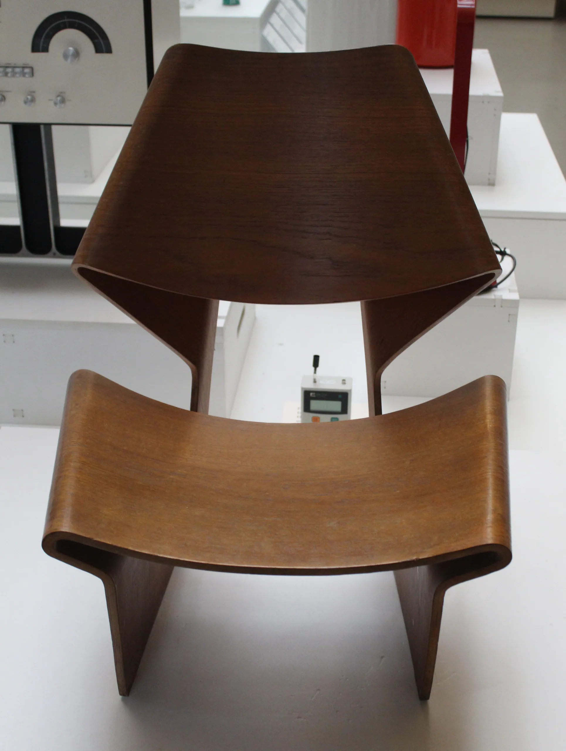 Front view of a brown moulded-plywood GJ Chair formed by two opposing curved shells in a museum display.