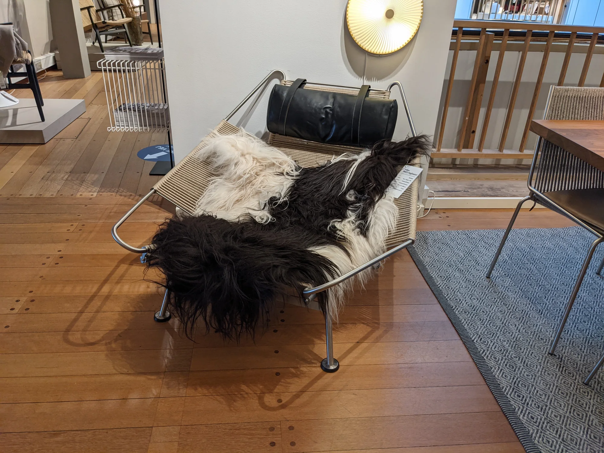 Three-quarter view of a Flag Halyard Chair in a shop, with a stainless-steel outline wrapped in natural cord, a black leather headrest and black-and-white sheepskin.
