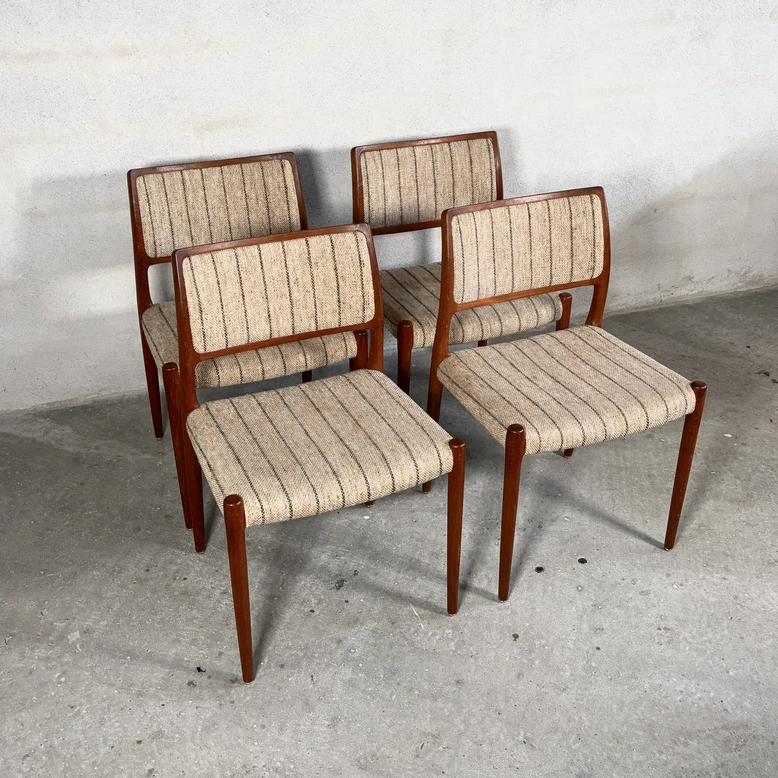 Four timber dining chairs have separate rectangular upholstered backs and seats in striped beige fabric, each panel held within a slender rounded frame.