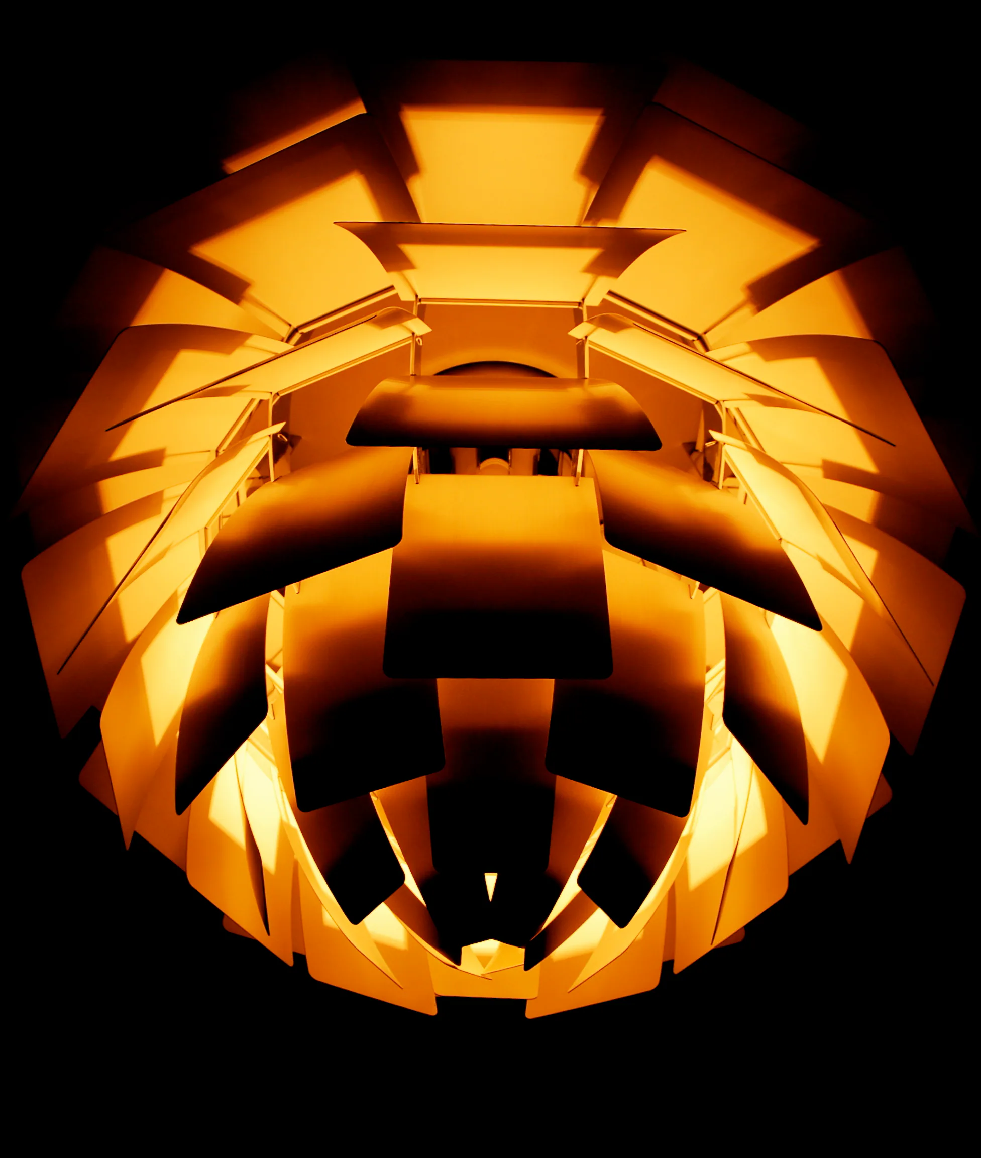 Upward view into a glowing copper PH Artichoke lamp, with overlapping metal leaves arranged around a concealed central light source.