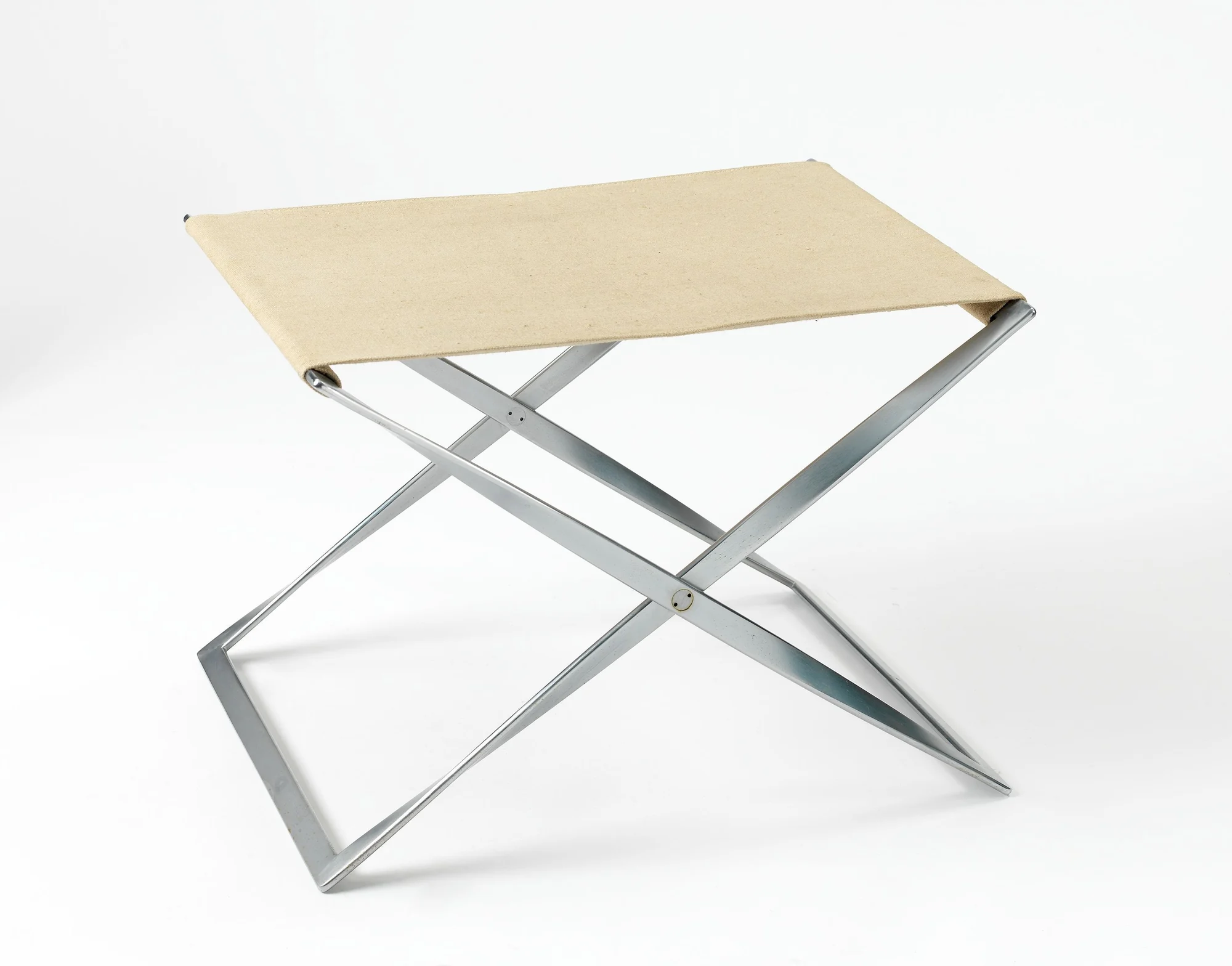 Three-quarter view of a PK91 folding stool with a pale canvas seat stretched across two crossing chrome-plated steel ribbon frames.