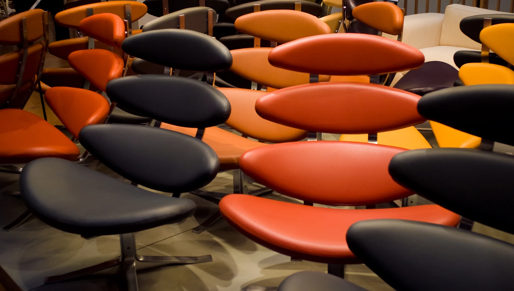 A dense display of red, orange and black Corona chairs, each with four separated elliptical upholstered pads rising from a central steel support.