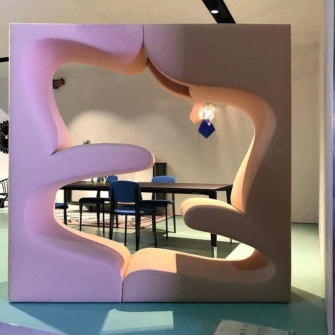Front view of a pale pink Living Tower with four curved upholstered seating levels arranged around a large opening through which a table and chairs remain visible.