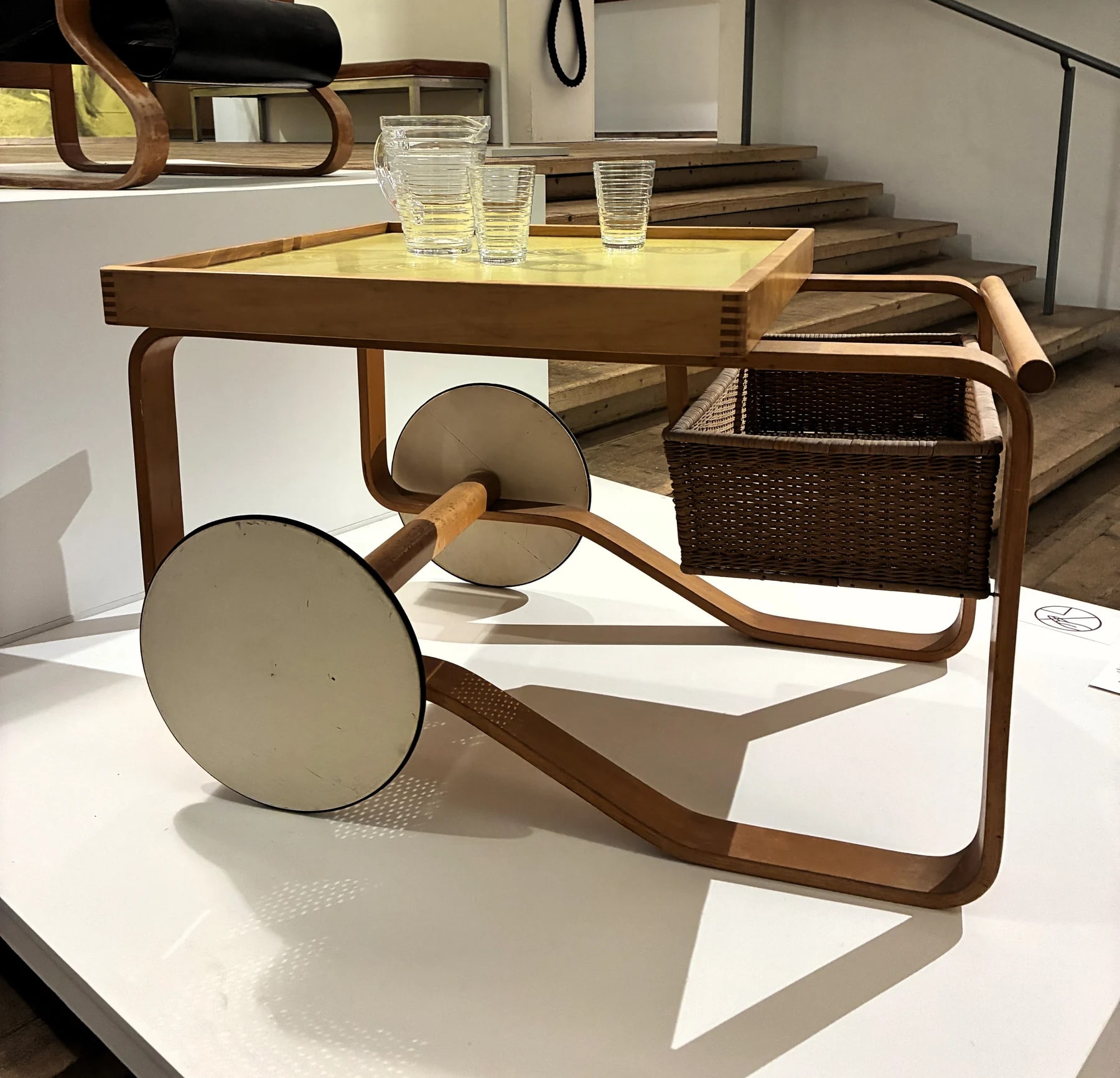 An Aalto tea trolley photographed at Millesgården, with a wood-rimmed tray, woven basket and large pale wheels; exact model uncertain.