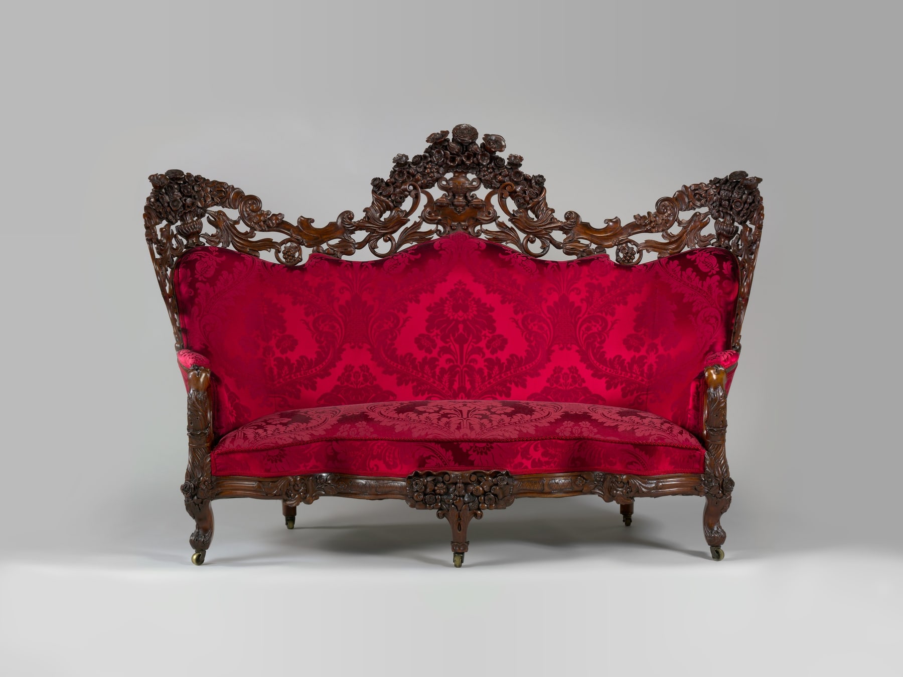 Belter sofa with a pierced rosewood crest and red modern upholstery framed by elaborate carving.