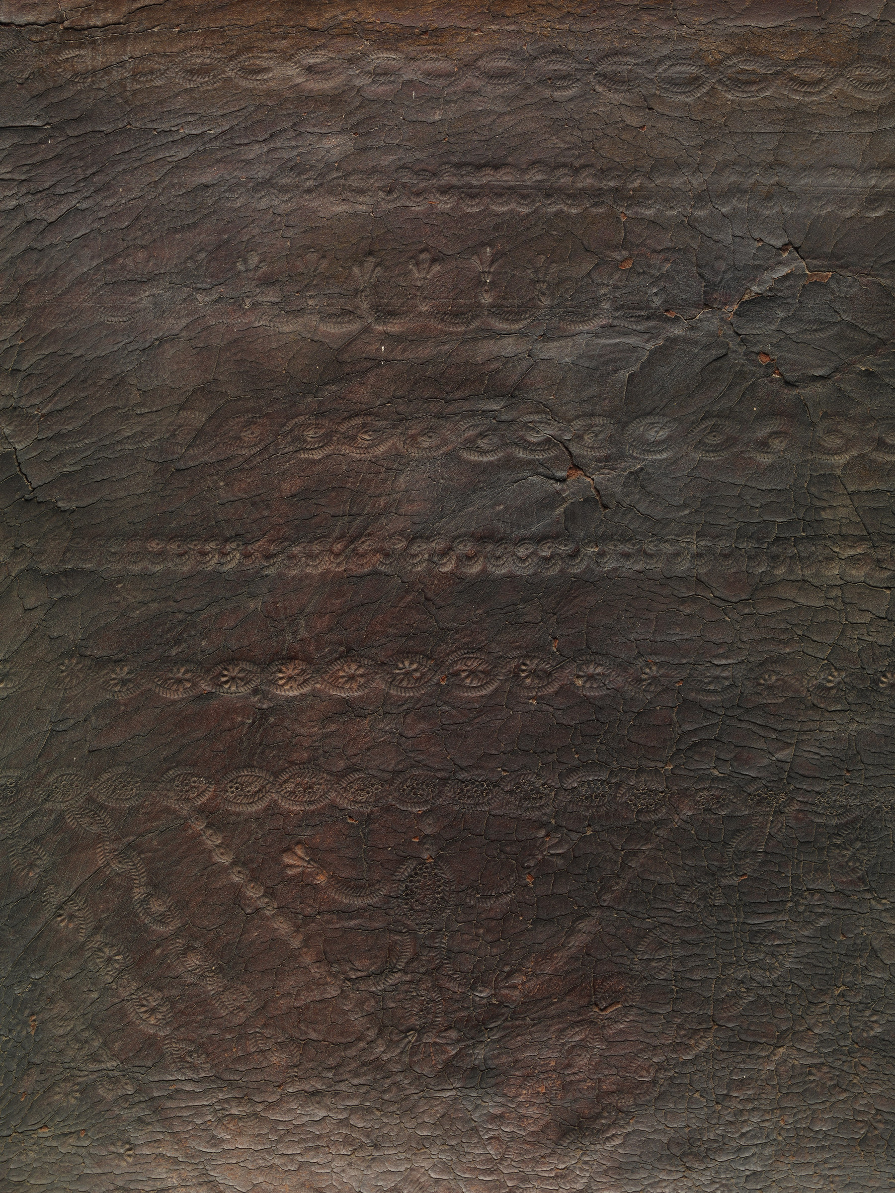 Close view of the chair's dark embossed leather showing a worn patterned field crossed by wrinkles, cracks and changes in sheen.