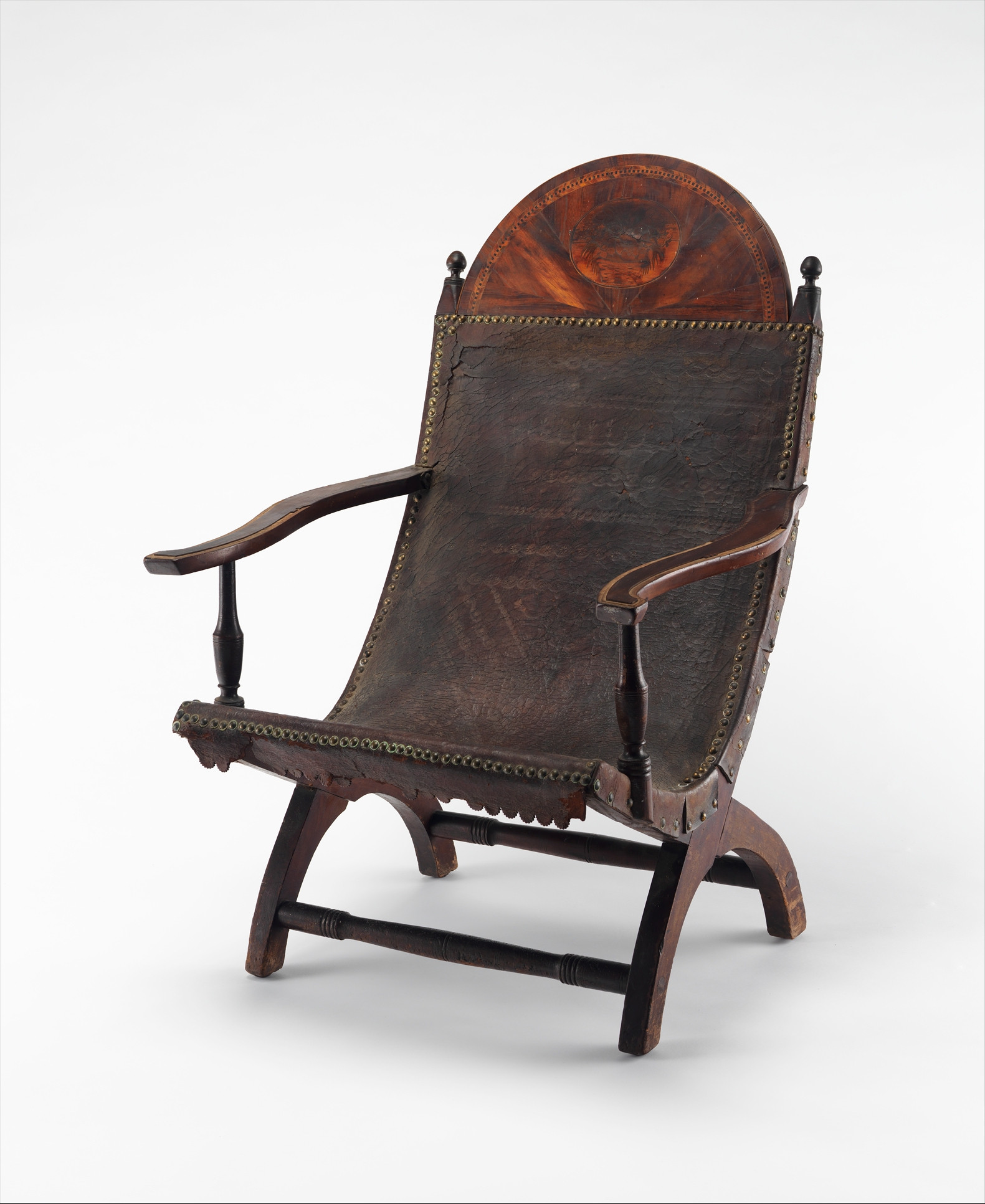Three-quarter view of a low reclining Campeche chair with dark leather, crossed side frames, curved arms and a half-round inlaid crest.