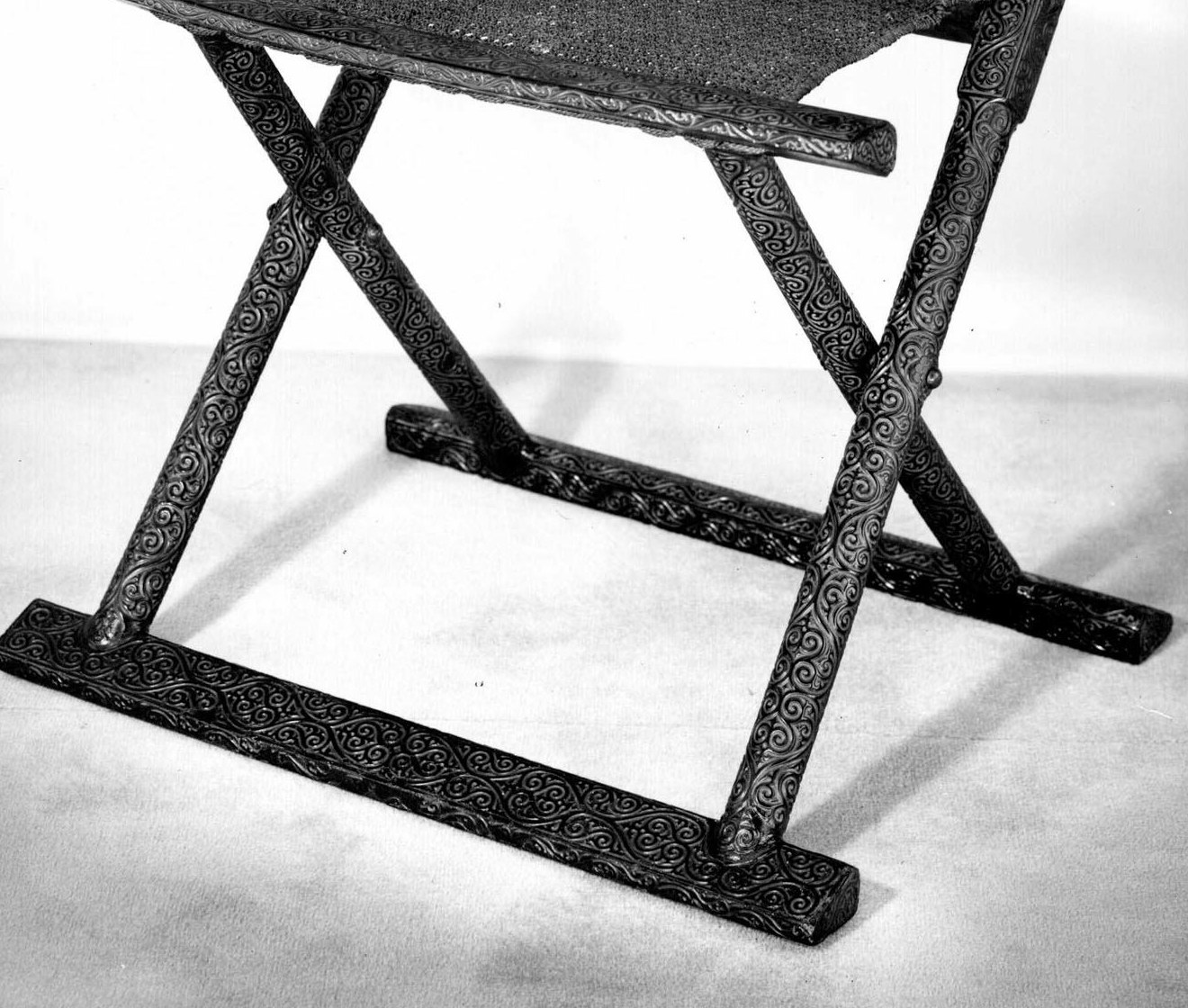 Lower detail of the Chinese chair showing its woven seat edge, paired crossed legs and long feet all bordered by dense carved scrollwork.
