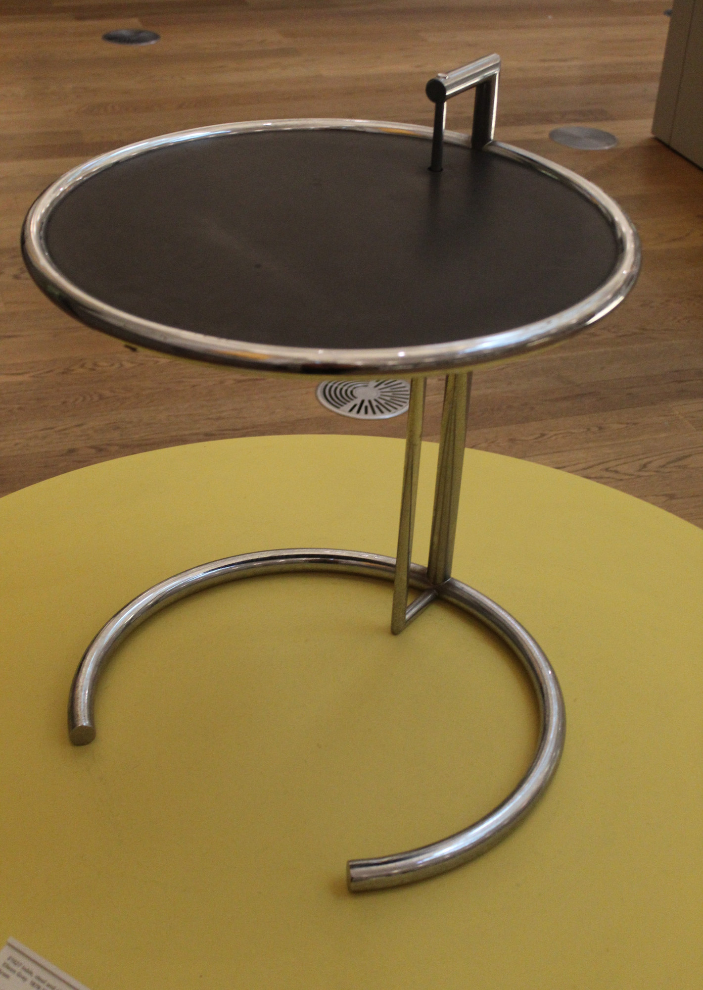 Closer three-quarter view of a later E-1027 table showing its open chrome base, twin uprights and raised handle above the circular top.