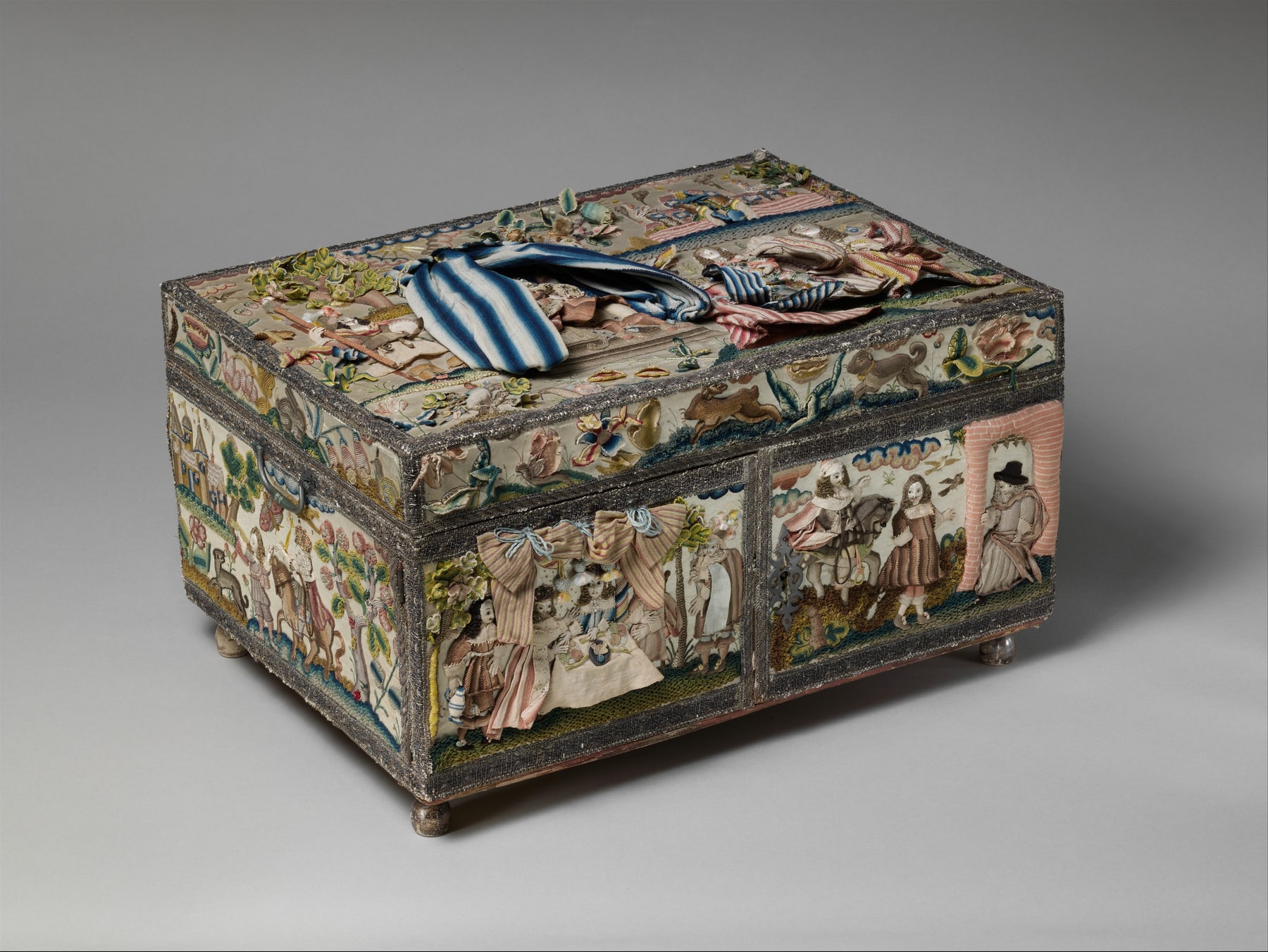 English embroidered cabinet with raised figures and landscapes across its closed exterior and lid.