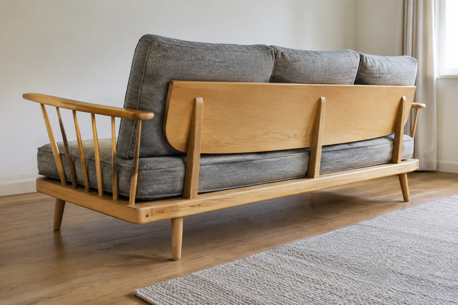 Reconstruction: The back and side of a wooden couch, showing its broad backboard, slender side spindles and separate grey cushions.