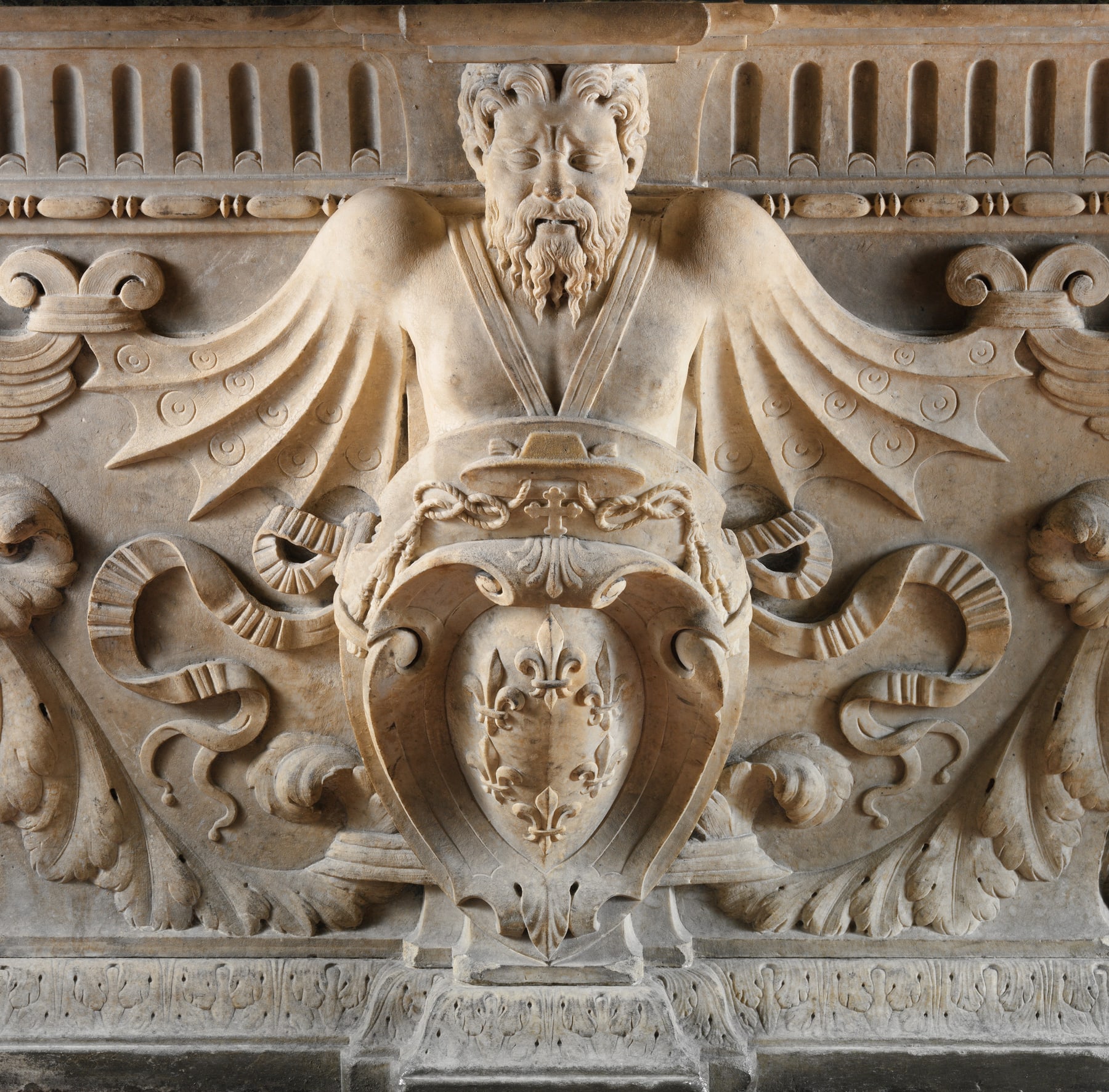 Close view of a Farnese Table support, with carved masks, wings and heraldic forms below the tabletop.