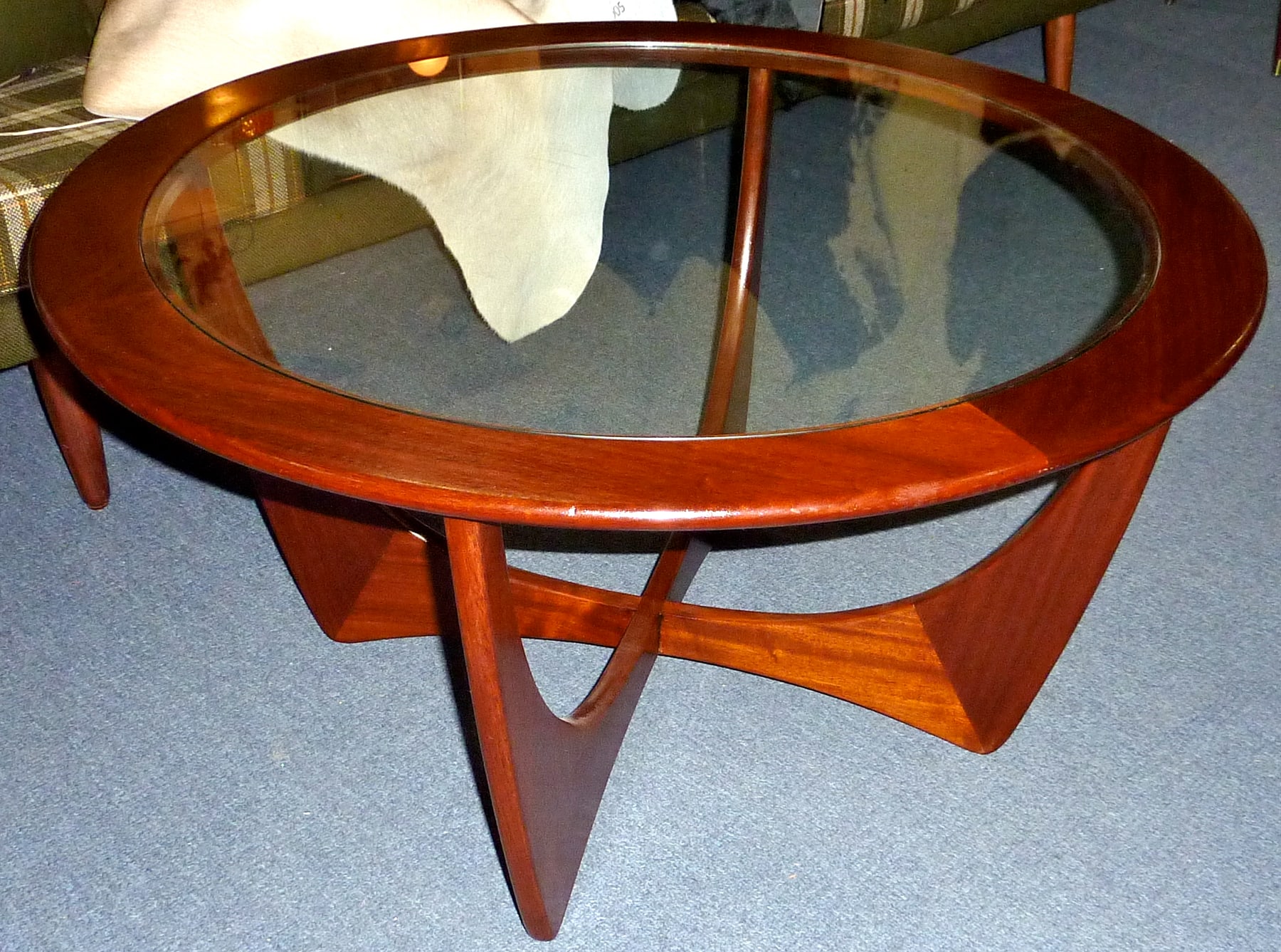 A round G Plan Astro coffee table with a wooden ring around a clear glass centre and curved wooden supports joined beneath it.