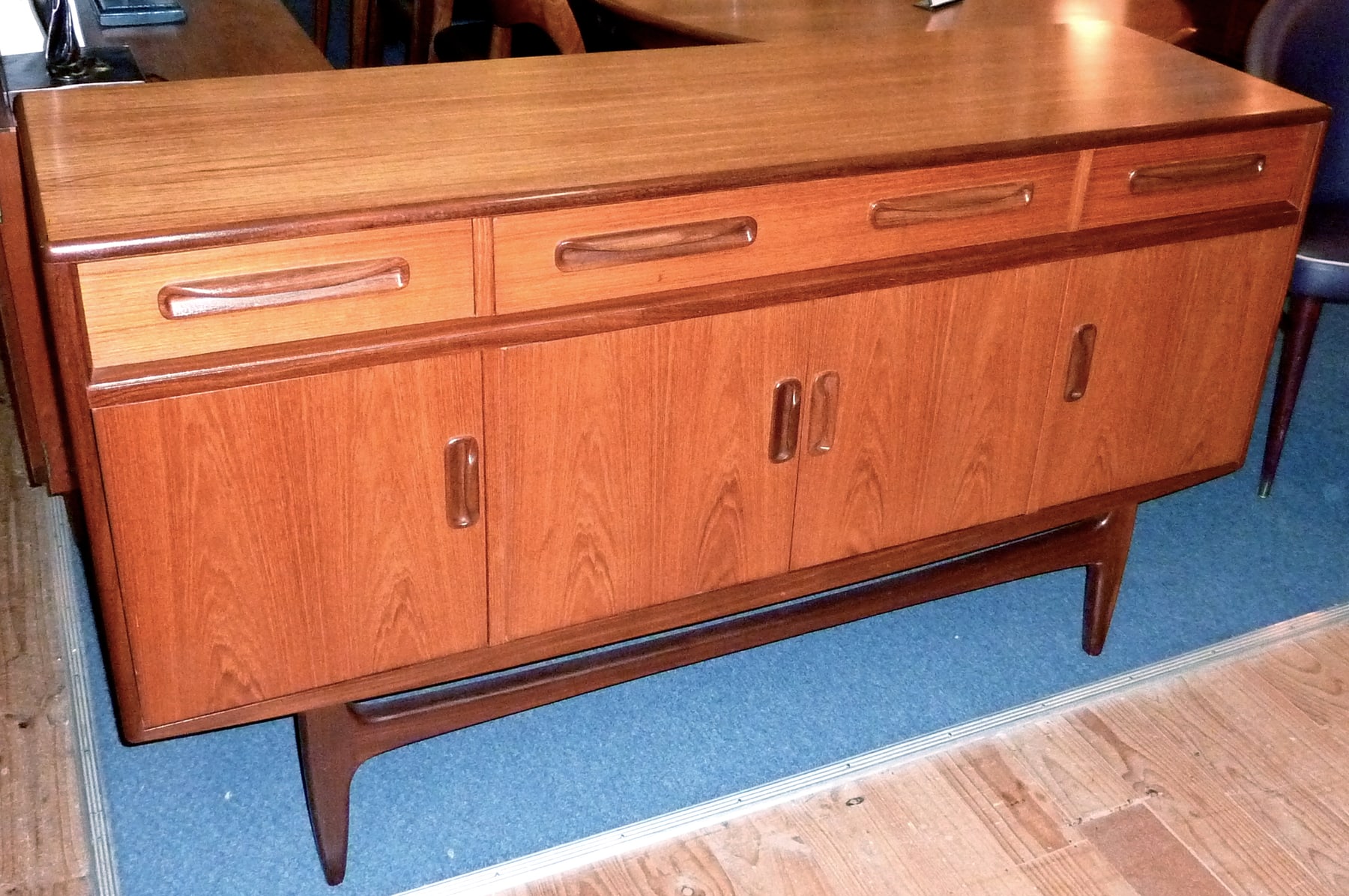 A teak G Plan Fresco sideboard with shaped drawer pulls, three doors and an open wooden base.