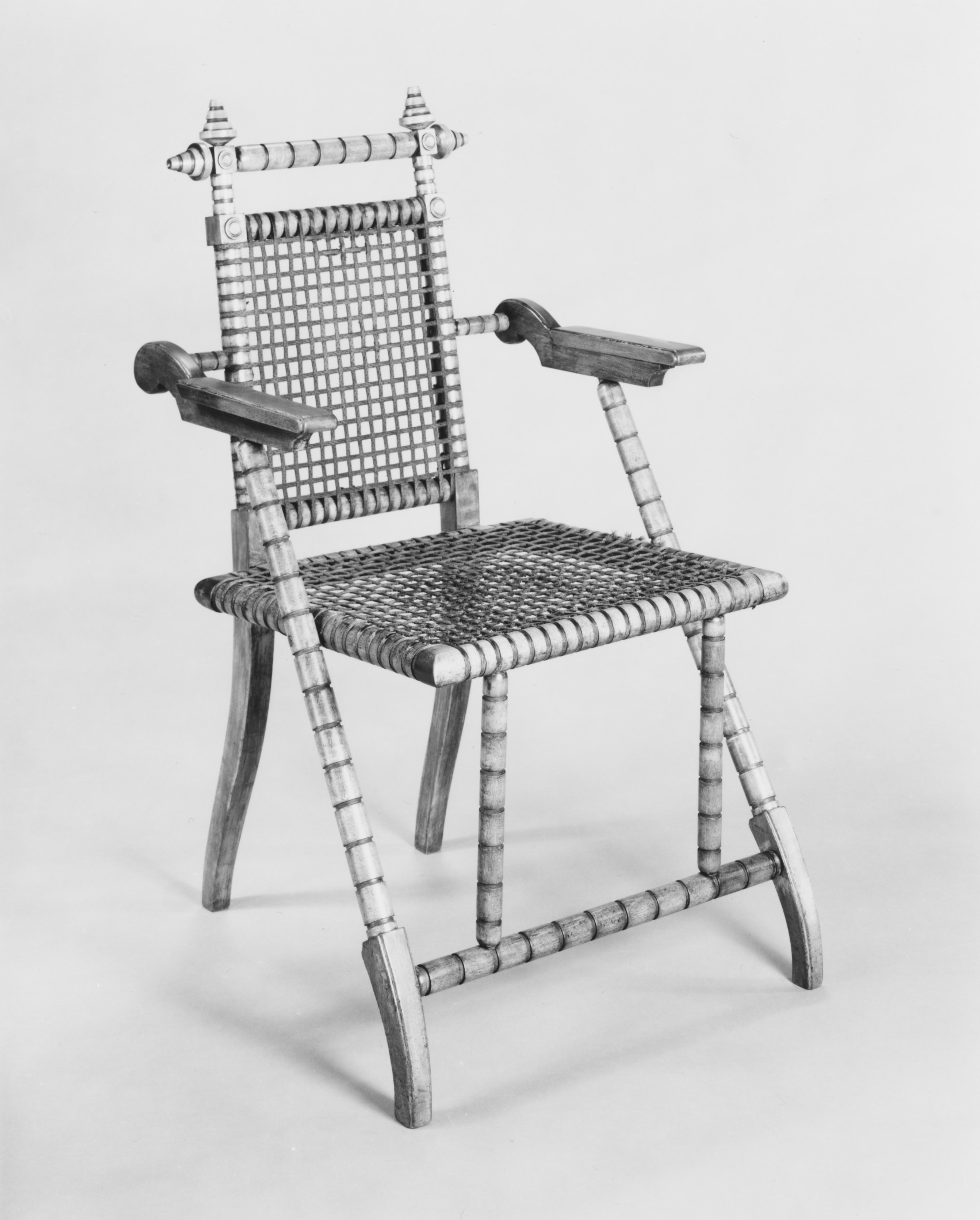 Three-quarter view of a light wooden folding armchair with a square woven grid across its seat and back.