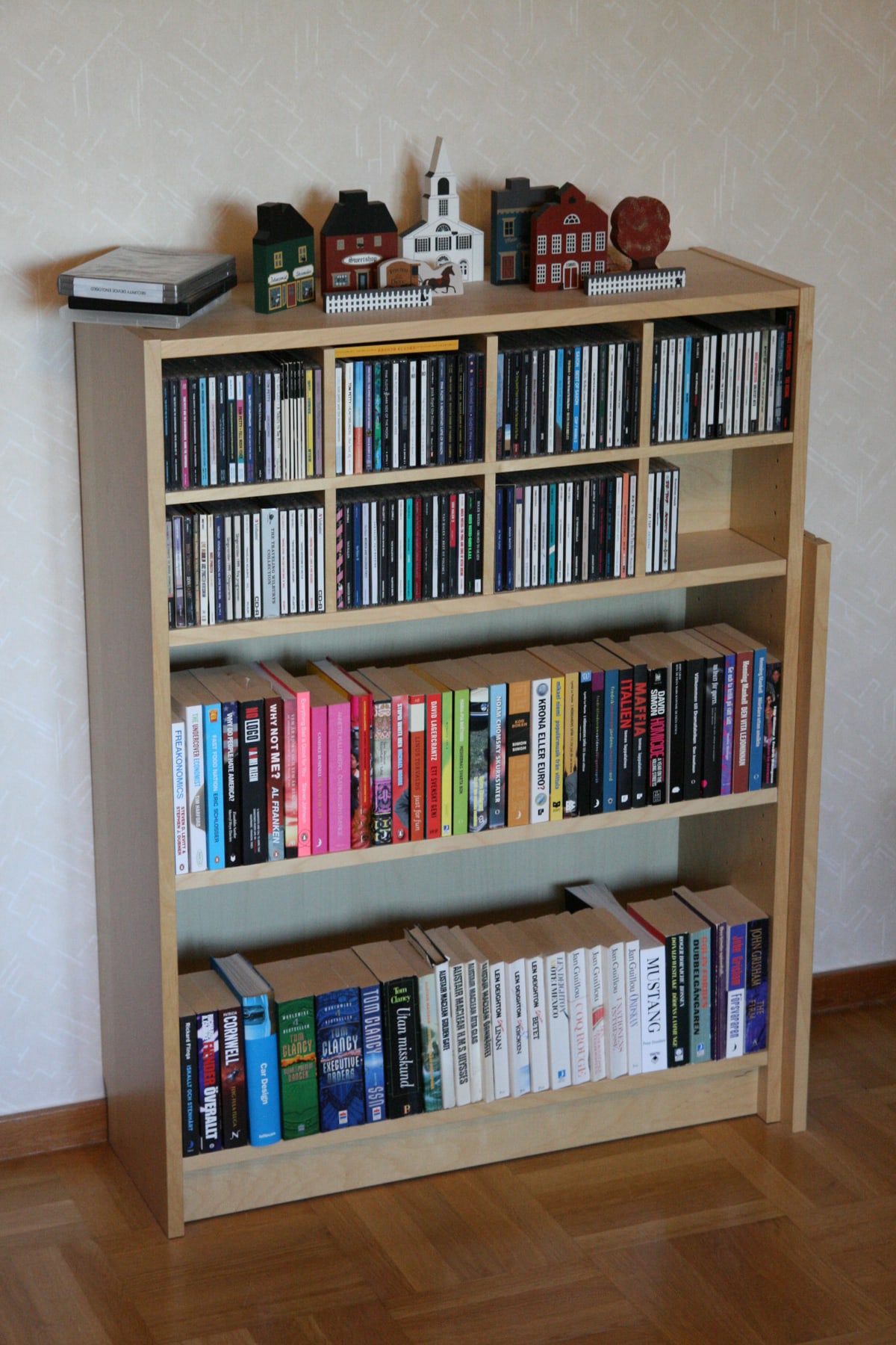 A low birch-veneer BILLY bookcase filled with books and CDs, with a spare shelf leaning against its side.