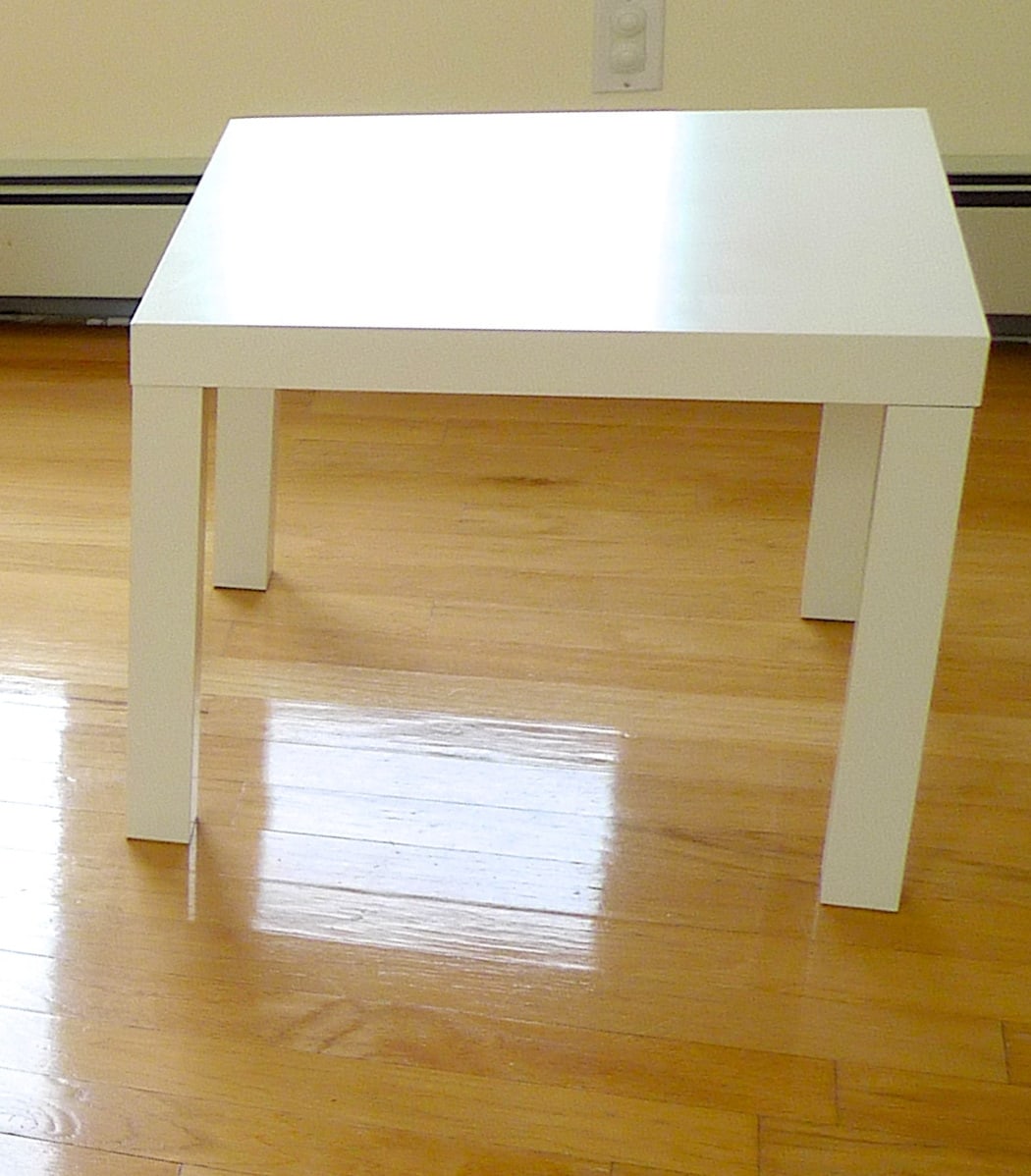A white square LACK side table with four thick rectangular legs beneath a similarly thick top.
