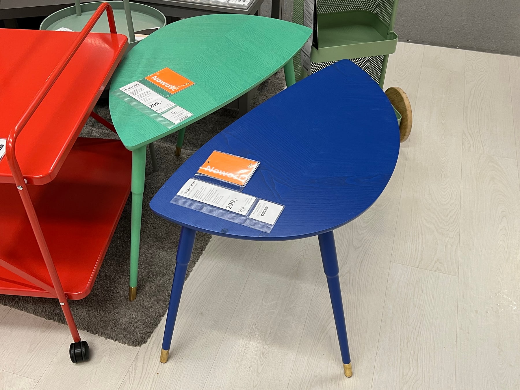 Green and blue LÖVBACKEN side tables on an IKEA shop display, with leaf-shaped tops and three slender legs with brass-coloured tips.