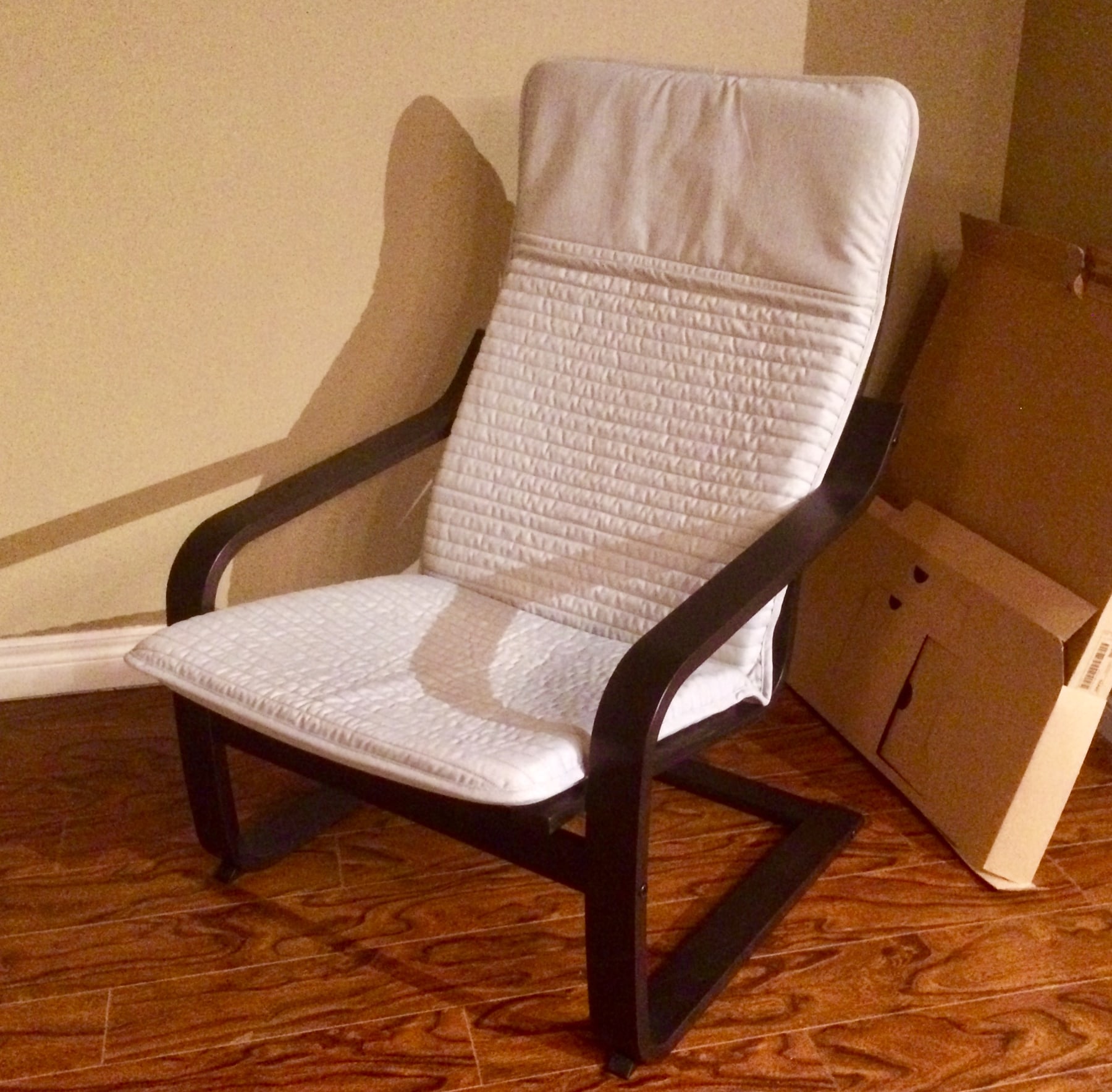 A POÄNG armchair with a dark curved wooden frame and beige cushion, its open side revealing the cantilever support.