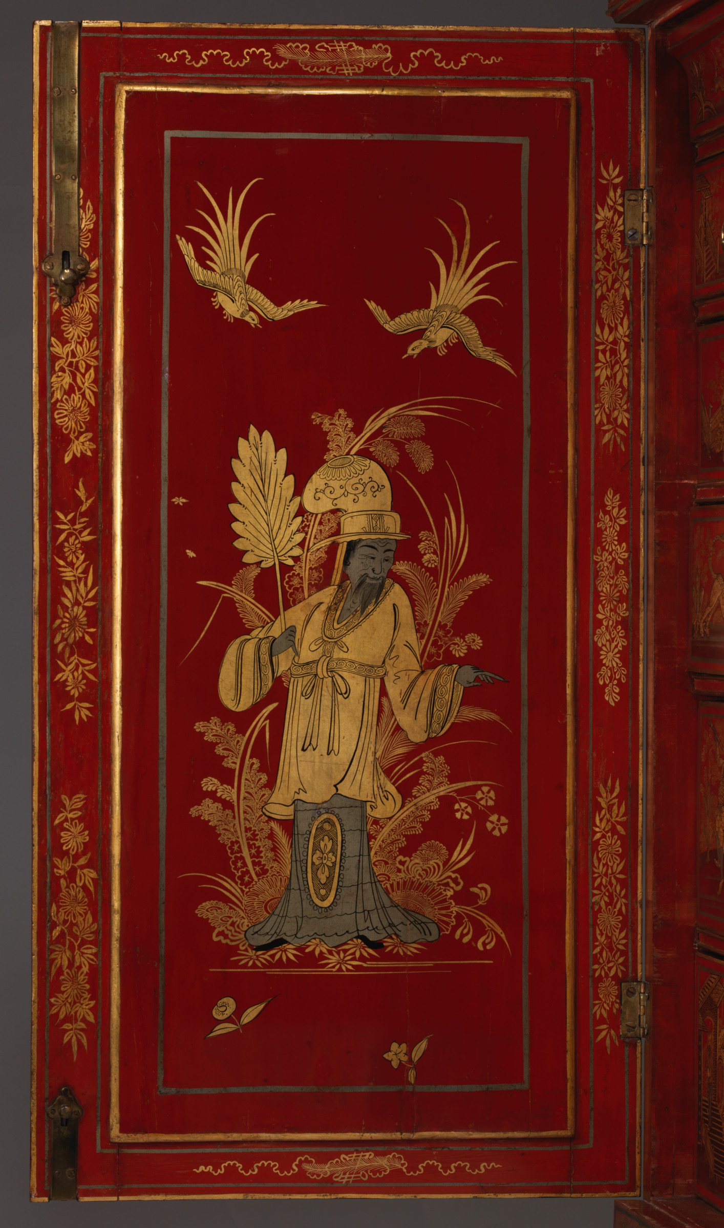 Close view of one red cabinet door with a gold-robed figure, birds and plants enclosed by fine borders beside hinges and a lock plate.