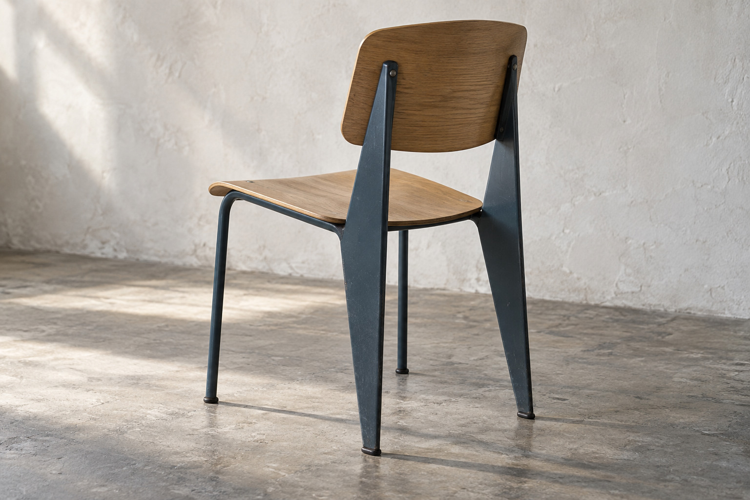 An interpreted rear view of a steel-and-plywood chair, showing two broad tapered rear supports and two slender tubular front legs in side light.