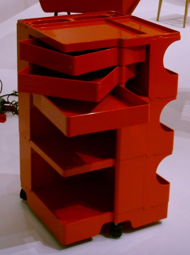 A red Boby storage trolley with three shallow trays swung open beside its deeper open compartments and small castors.