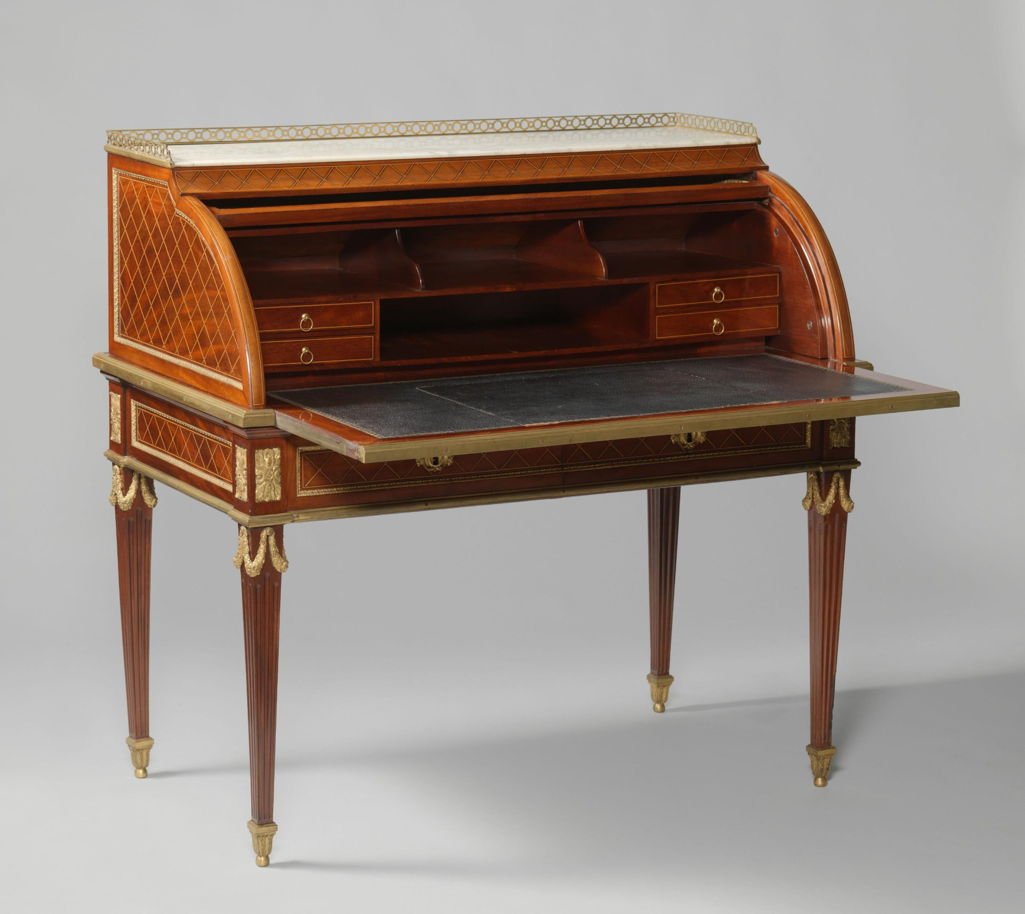 Open cylinder-top desk seen in perspective with the leather writing slide extended and fitted shelves and small drawers exposed.