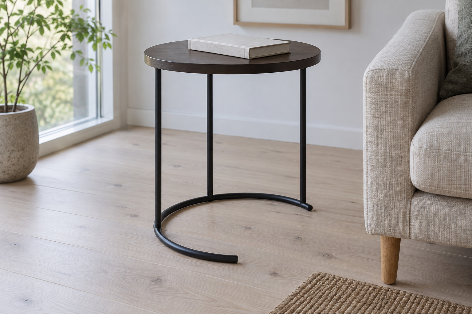 A small round dark table has three slender uprights and an open C-shaped floor base beside an upholstered chair.
