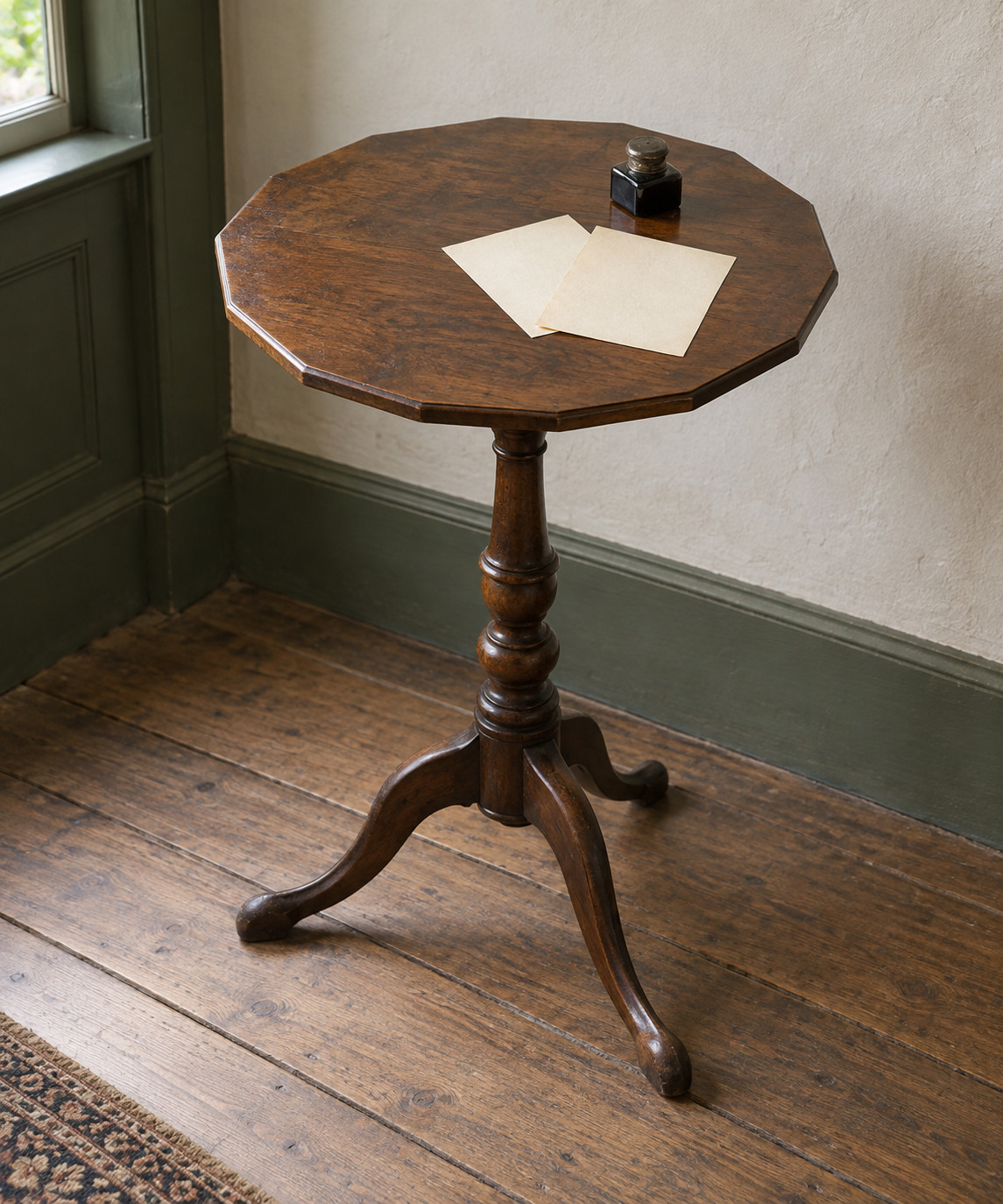 A small many-sided dark wooden top stands on a central turned support with three spreading feet; two small sheets and an ink bottle sit above.