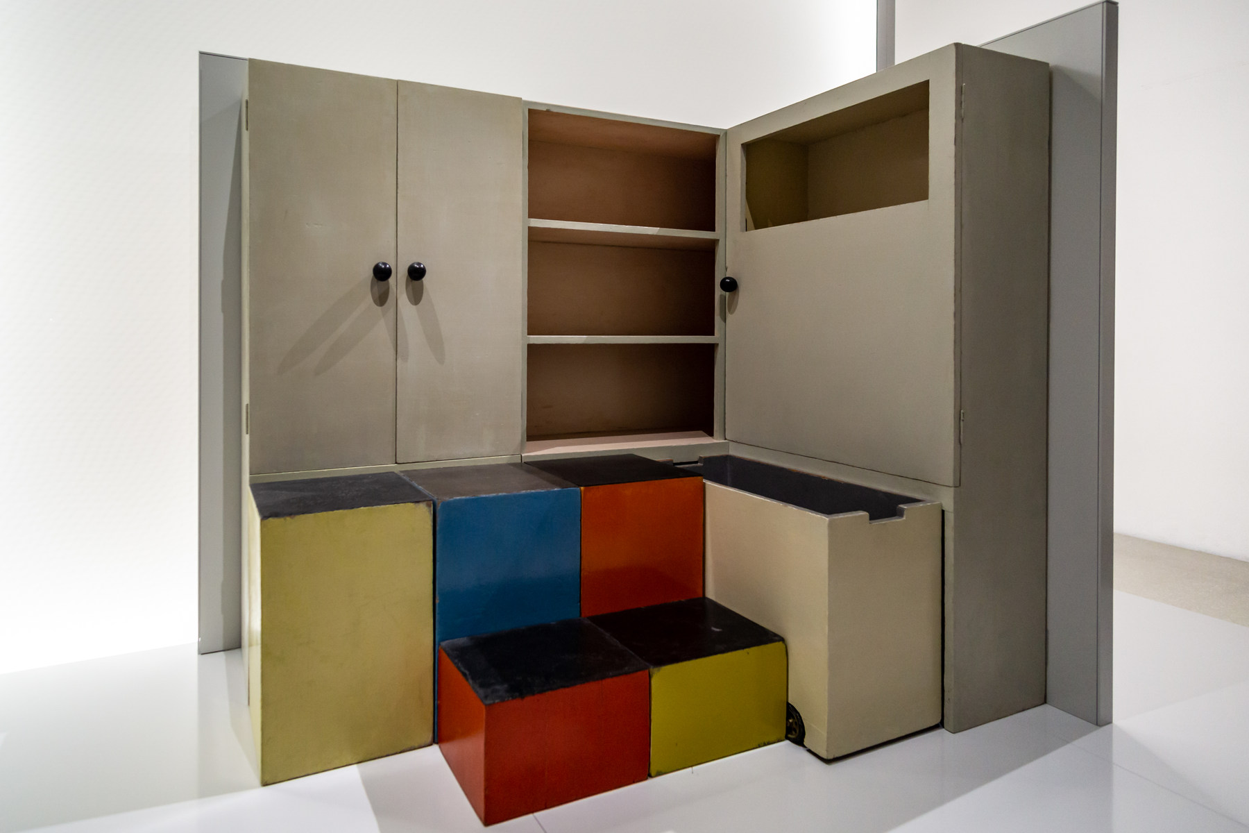 The TI 24 cupboard in a museum display has pale doors and shelves with blue, red and yellow removable boxes pulled forward.