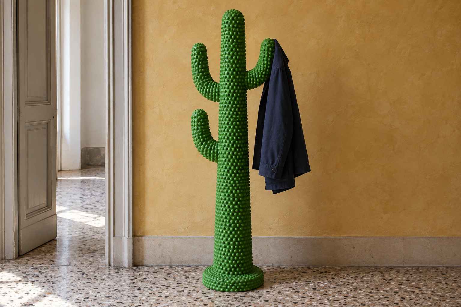 A green cactus-shaped coat stand with a bumpy surface holds one dark coat in an uncluttered hallway.