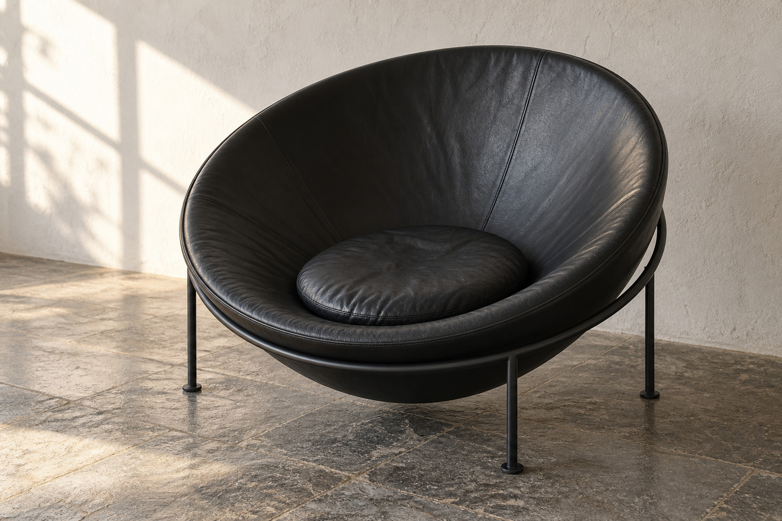 A black upholstered hemispherical chair rests at a tilt within a thin metal ring on slender legs.