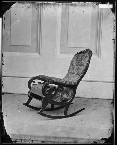 An early monochrome photograph isolates the empty Lincoln rocker against a panelled wall, showing the curved wooden frame and upholstered seat and back.