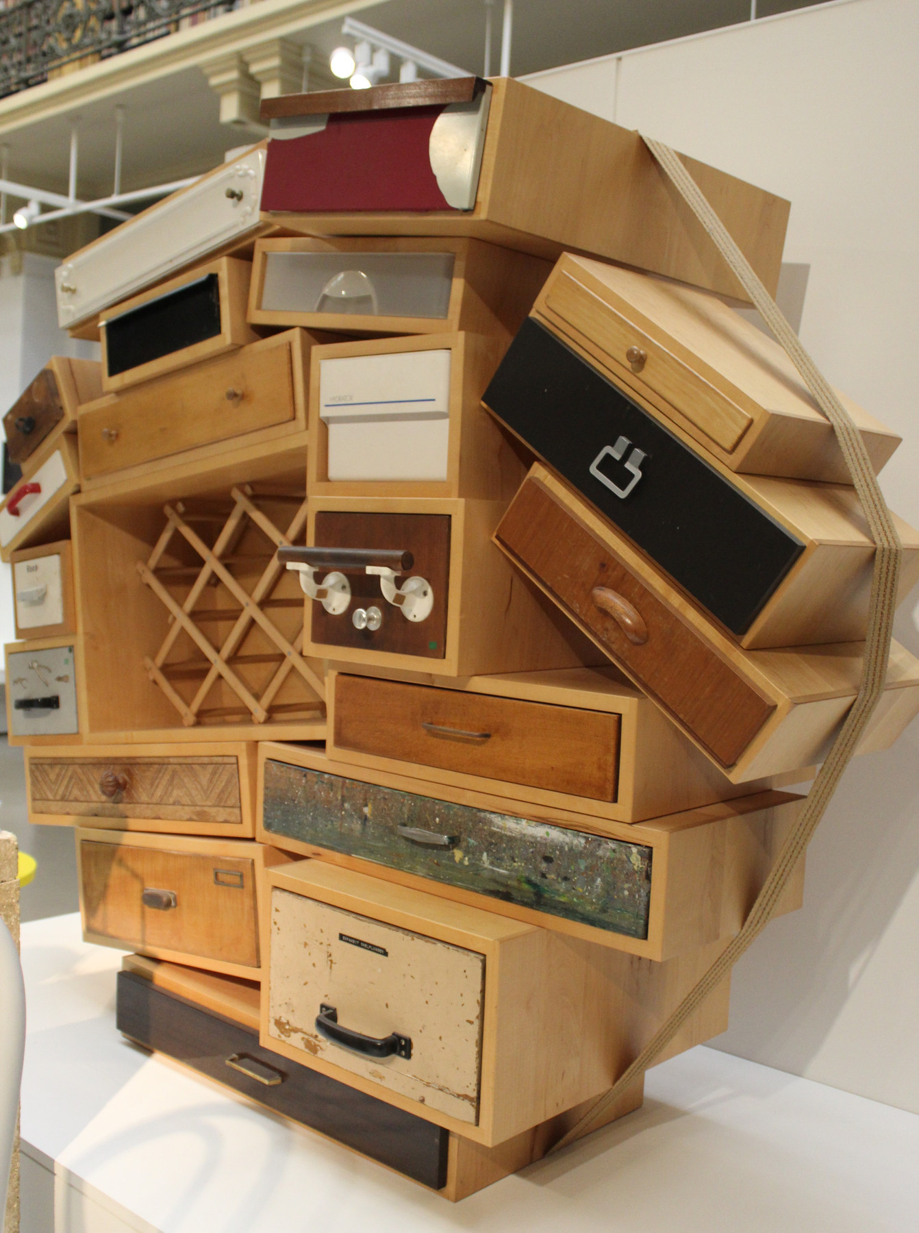 Found drawer fronts in individual pale wood housings form an irregular chest, gathered by a strap at the Victoria and Albert Museum.