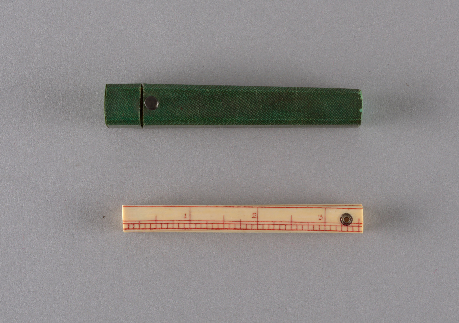 A small green shagreen-covered case lies above a folded ivory ruler, showing the difference between the textured covering and the smooth instrument.