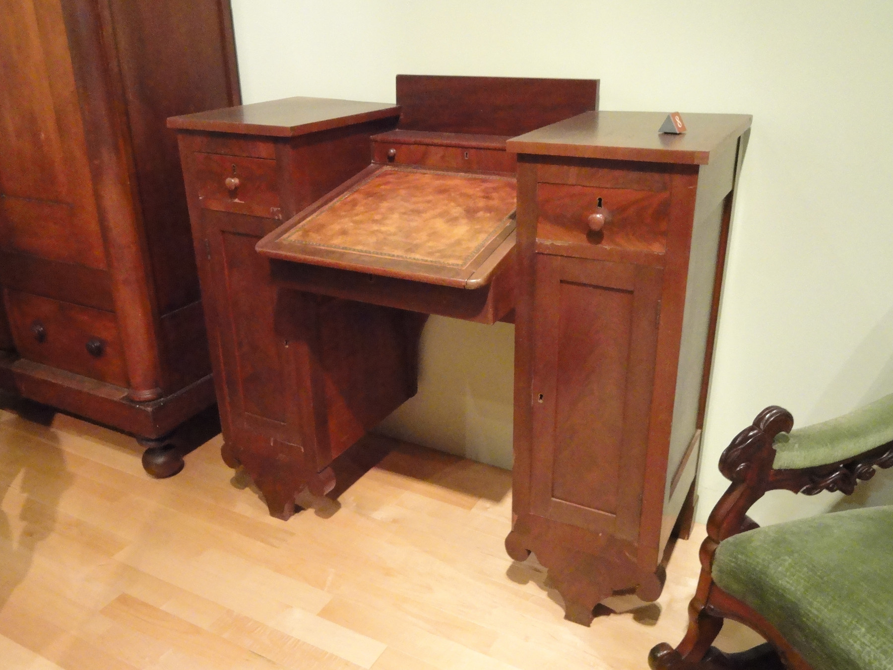 A writing desk has a sloped central surface between two tall storage sections, with strongly shaped feet below.