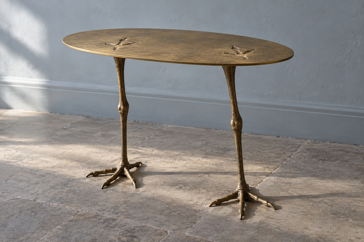 A small oval golden table stands on two bird-like legs, with two recessed footprint shapes on its top.