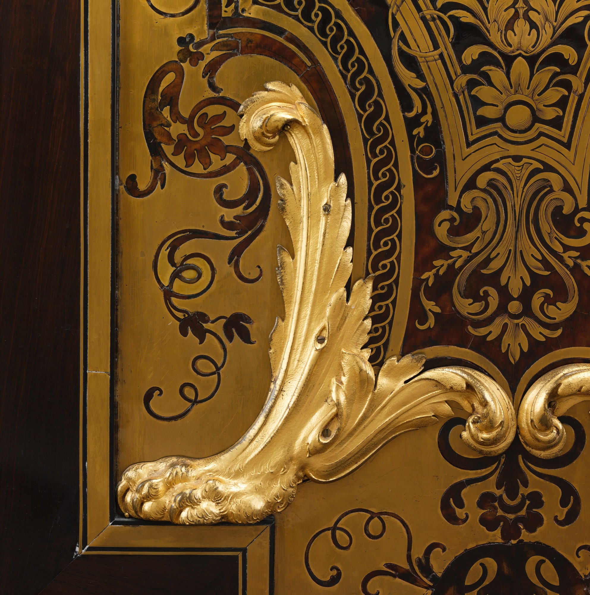 Close detail of brass and tortoiseshell marquetry beside a projecting gilt-bronze leaf mount on the Boulle-attributed cabinet.