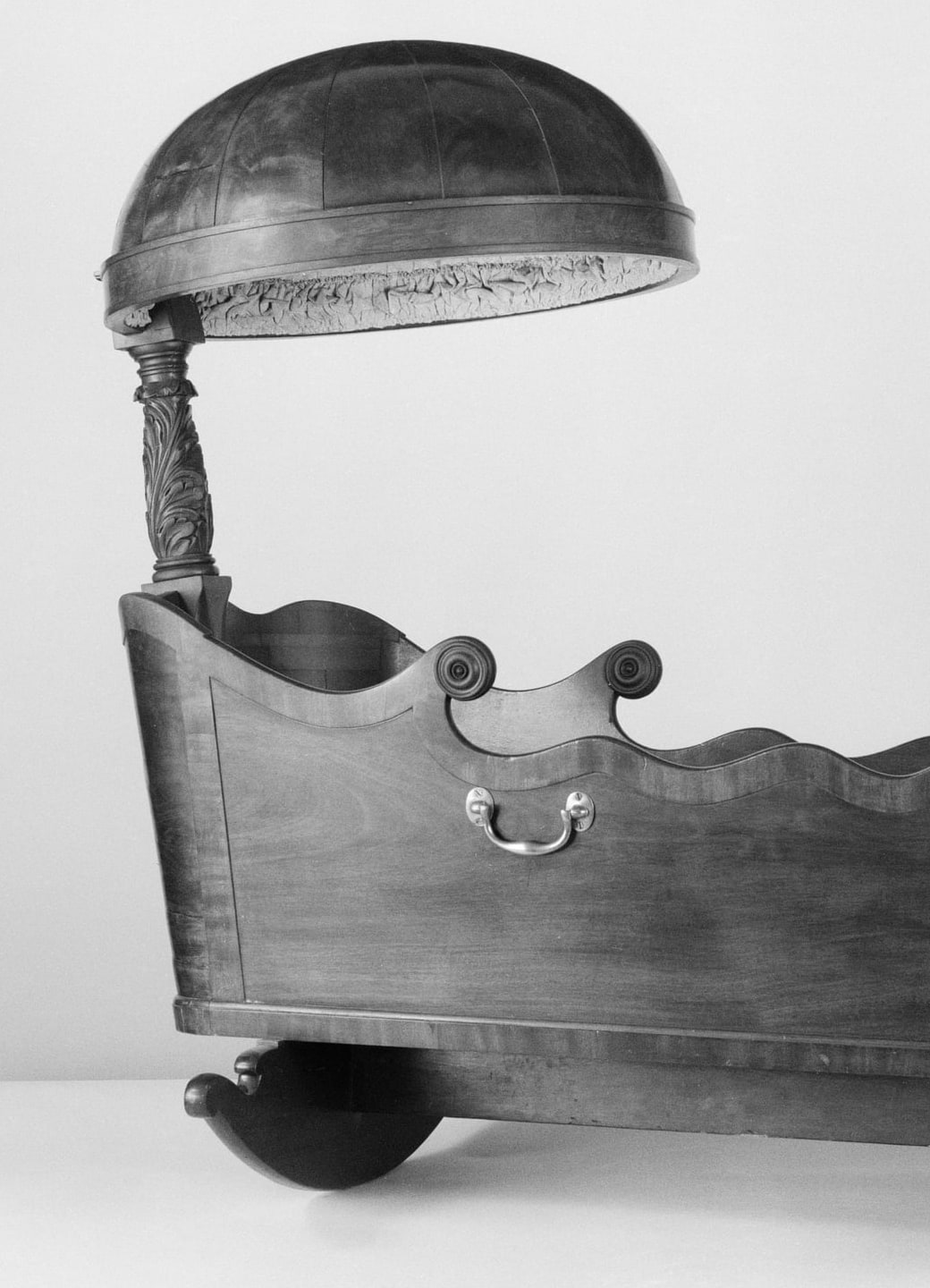 Cropped archival detail showing the cradle’s hood support, shaped rim and one rocker; the monochrome image does not record original colour.