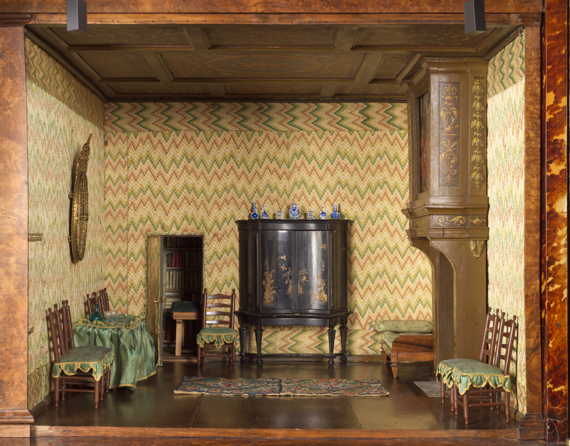 Lower-right room of Oortman's dolls' house with textile-covered walls, fireplace, black cabinet, small chairs and a carpet.