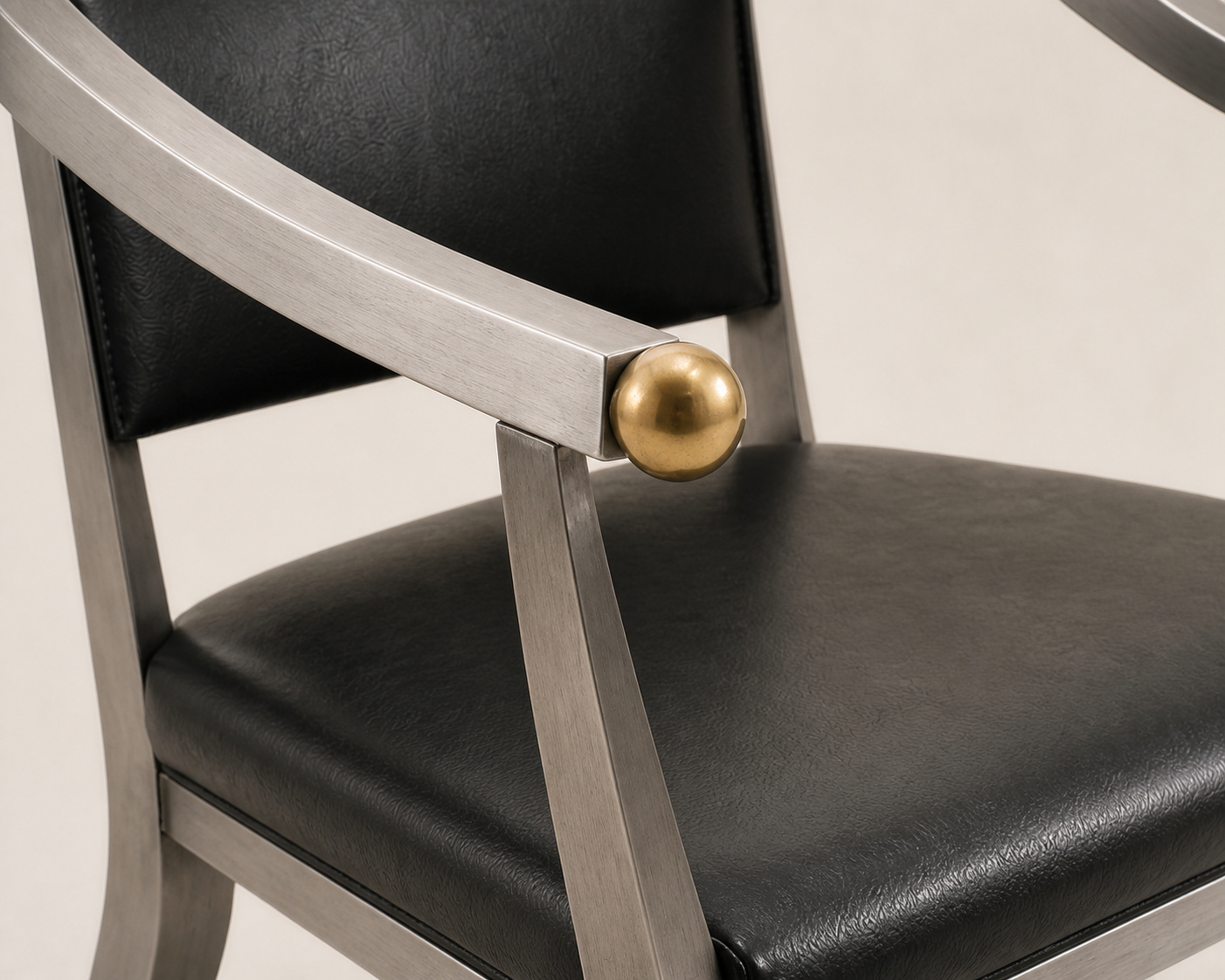 Close editorial reconstruction of a brushed-steel arm rail ending in a small brass sphere beside separate black leather back and seat planes.