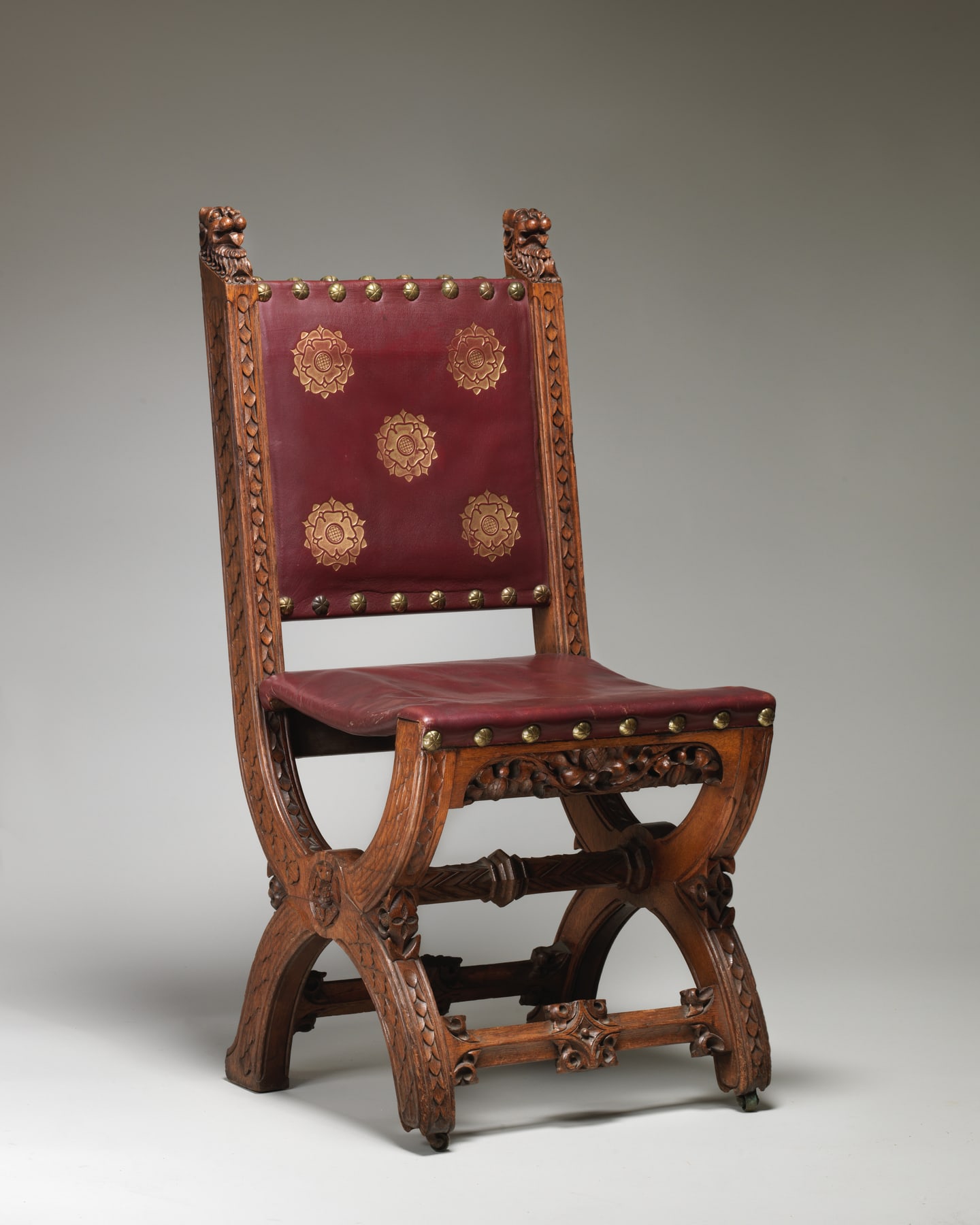 Pugin-designed Speaker’s House chair made by Holland & Sons in 1859, with a carved oak X-frame and modern red leather.