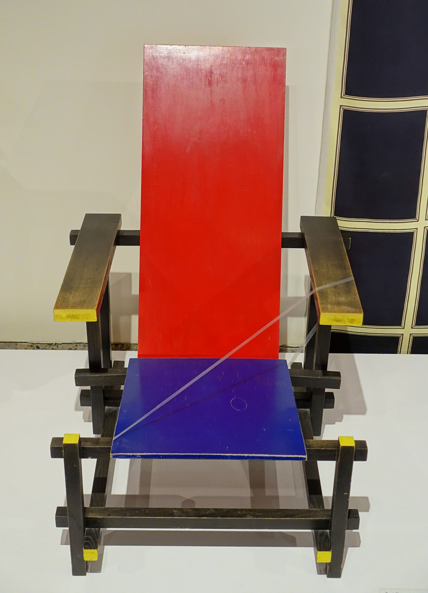 Frontal view of a worn 1960s Red Blue Chair museum example, showing its separate red back, blue seat and black wooden frame.