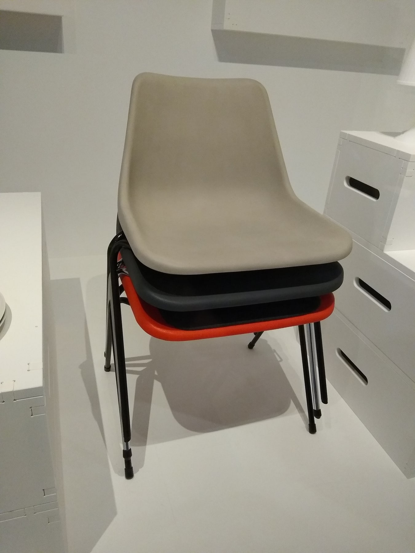 Four Robin Day polypropylene chairs stacked together, with pale, dark and red shells resting above thin metal legs.