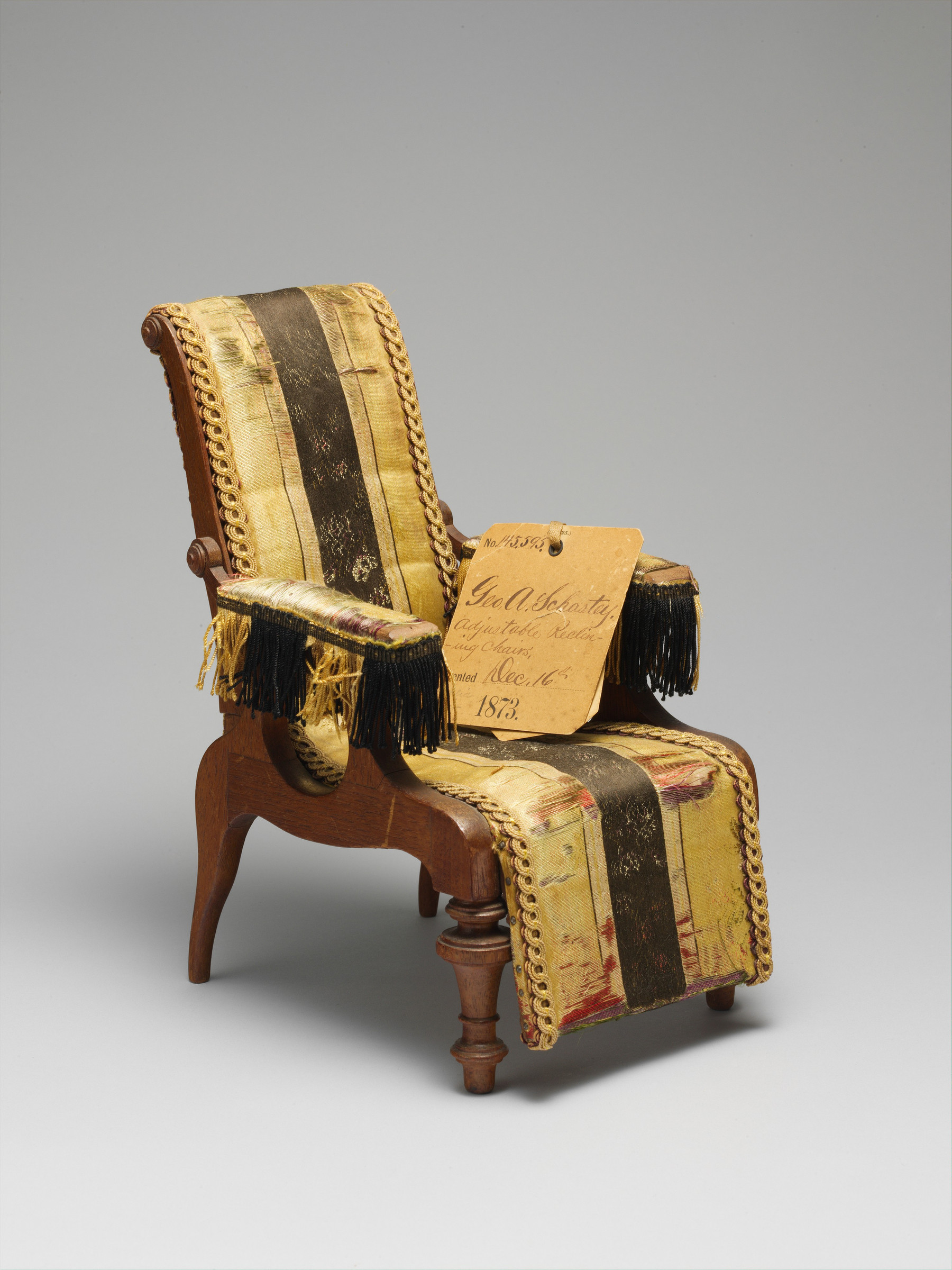 Three-quarter view of Schastey's small upholstered reclining-chair patent model with its handwritten 1873 identification tag.