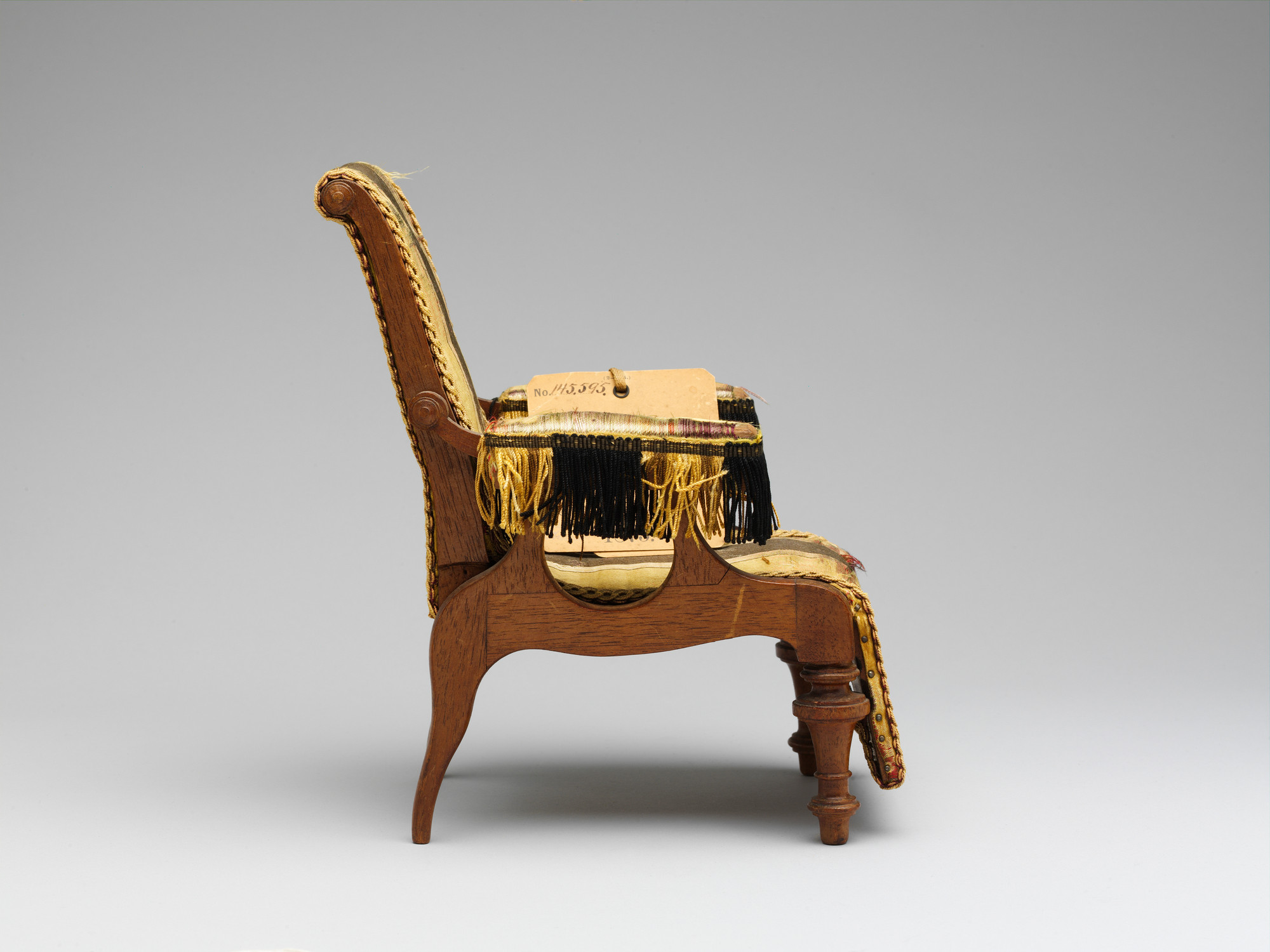 Side view of the small patent model showing its curved back, level upholstered arm, wooden links and extended leg support.
