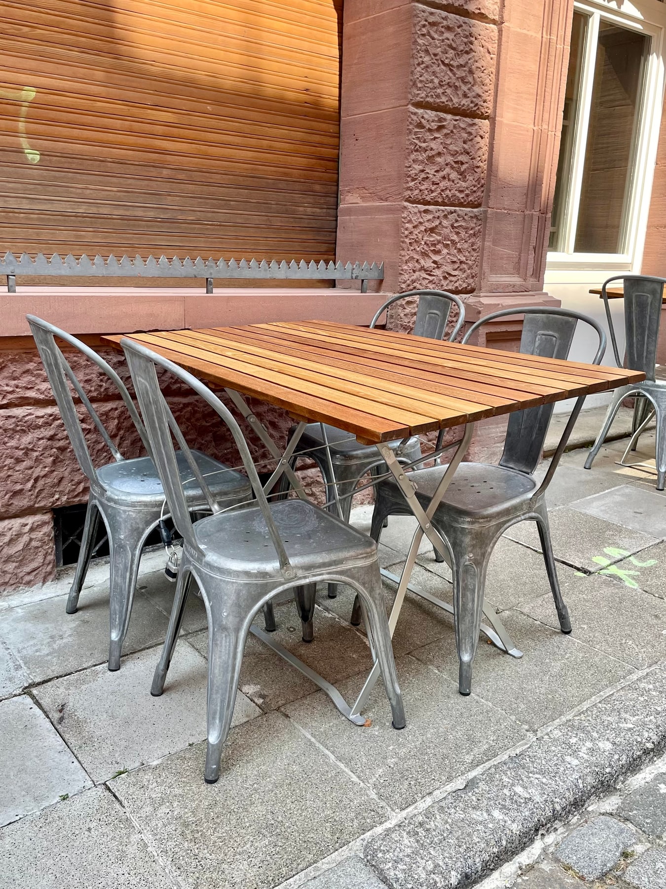 Metal Tolix Chair A chairs arranged around a wooden café table outside a brick building.